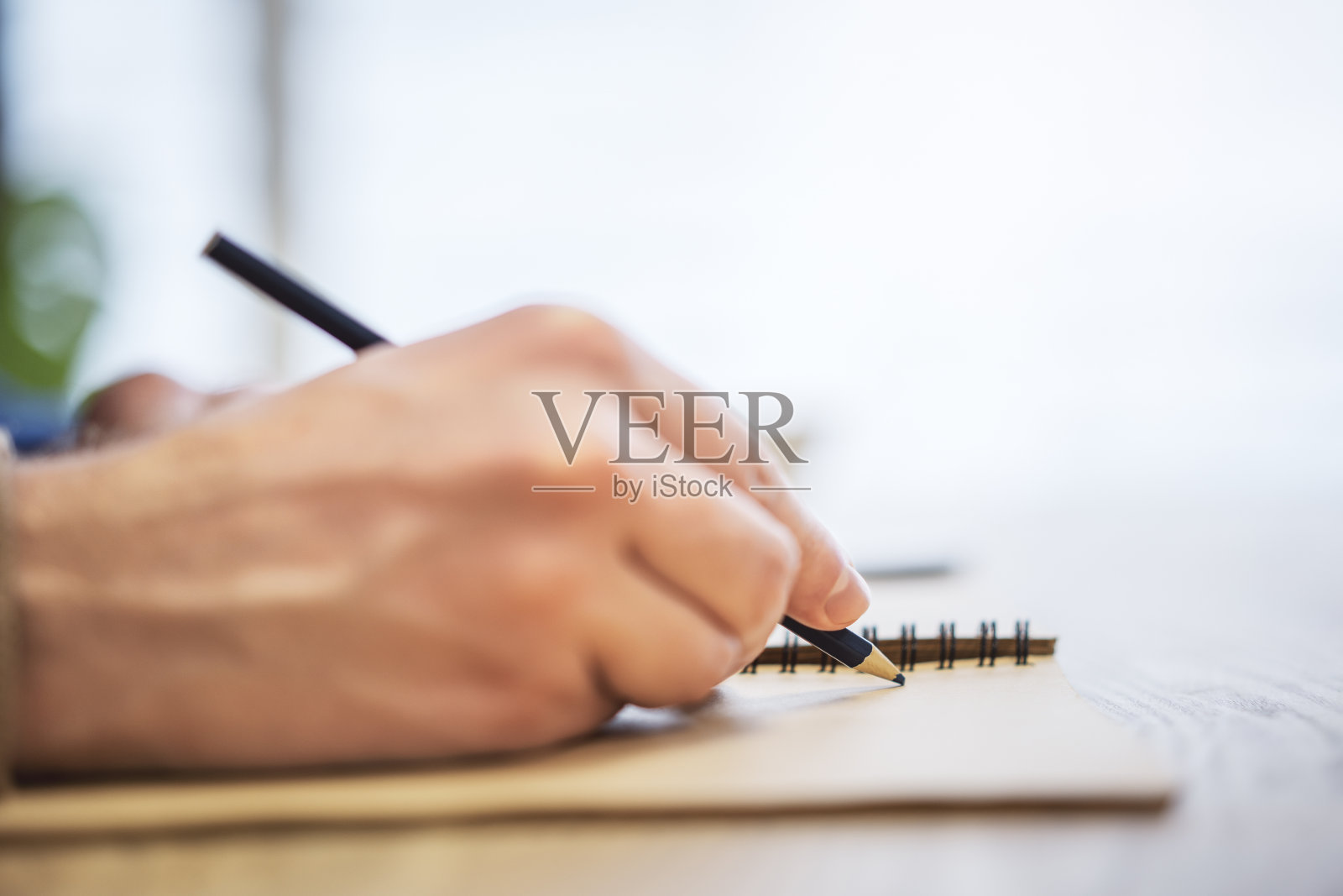 一个人的手在记事本上写条目的近景，周围有柔和的模糊照片摄影图片