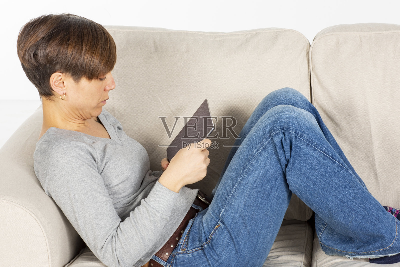 女人放松地躺在家里的沙发上看数码平板电脑。照片摄影图片