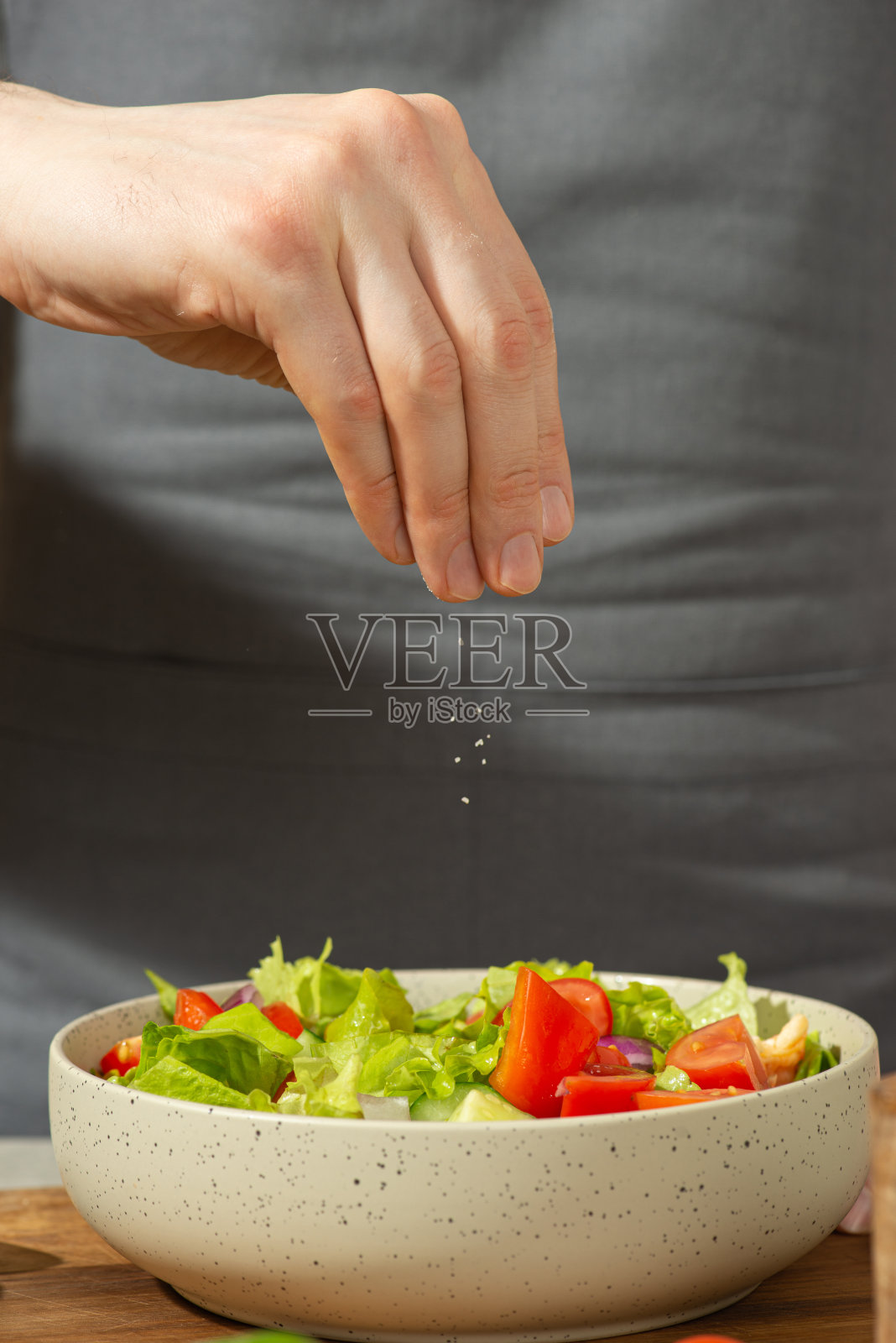 一个男人系着围裙准备蔬菜沙拉(特写)照片摄影图片