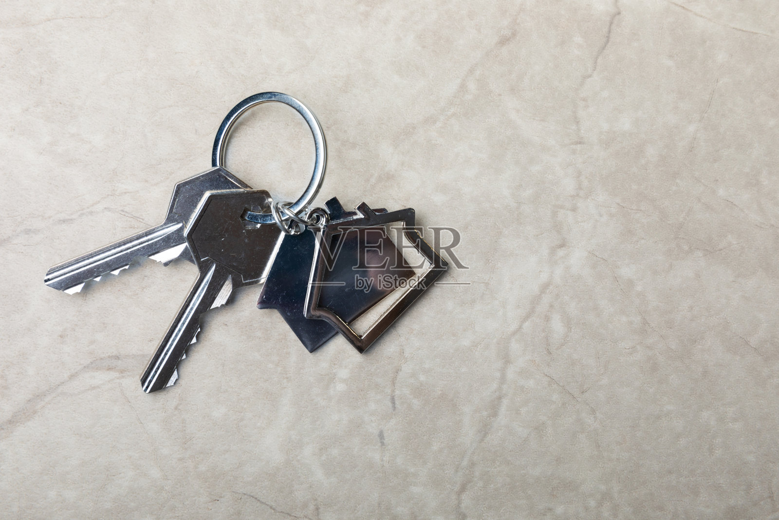 带钥匙链的房子形状的钥匙。灰色大理石背景上的构图。设计元素。房地产和保险概念。复制的地方。照片摄影图片