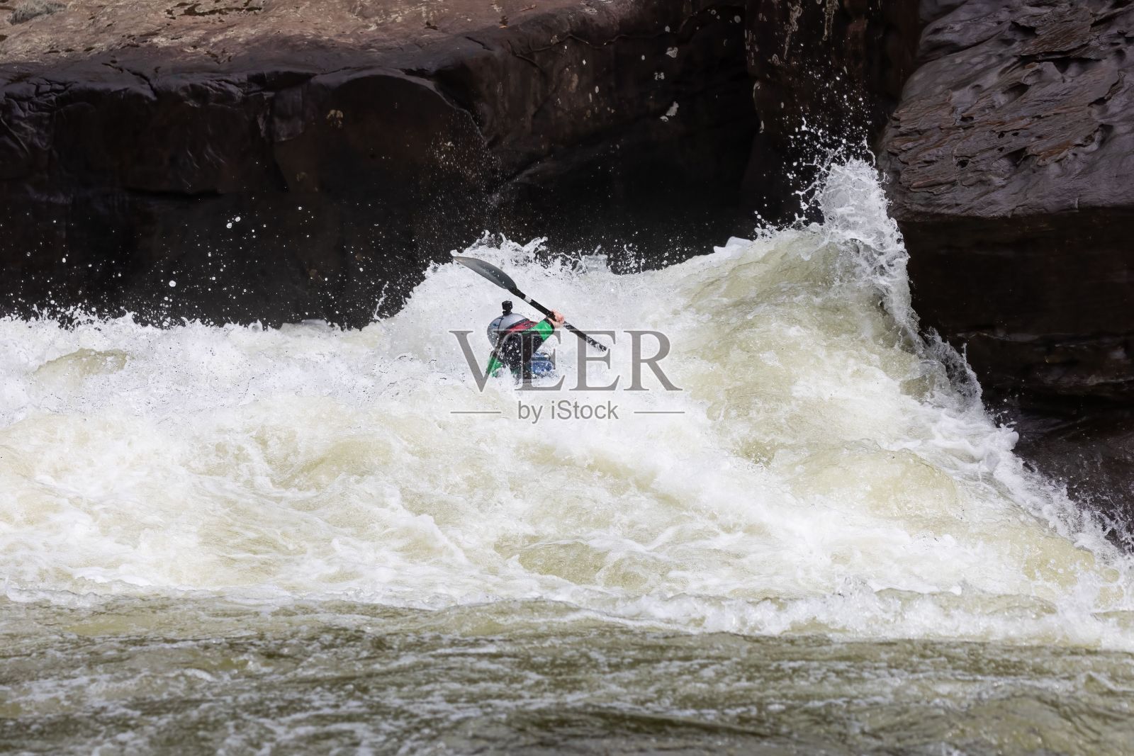 一个人在汹涌的河水中划皮艇，周围都是巨石。照片摄影图片