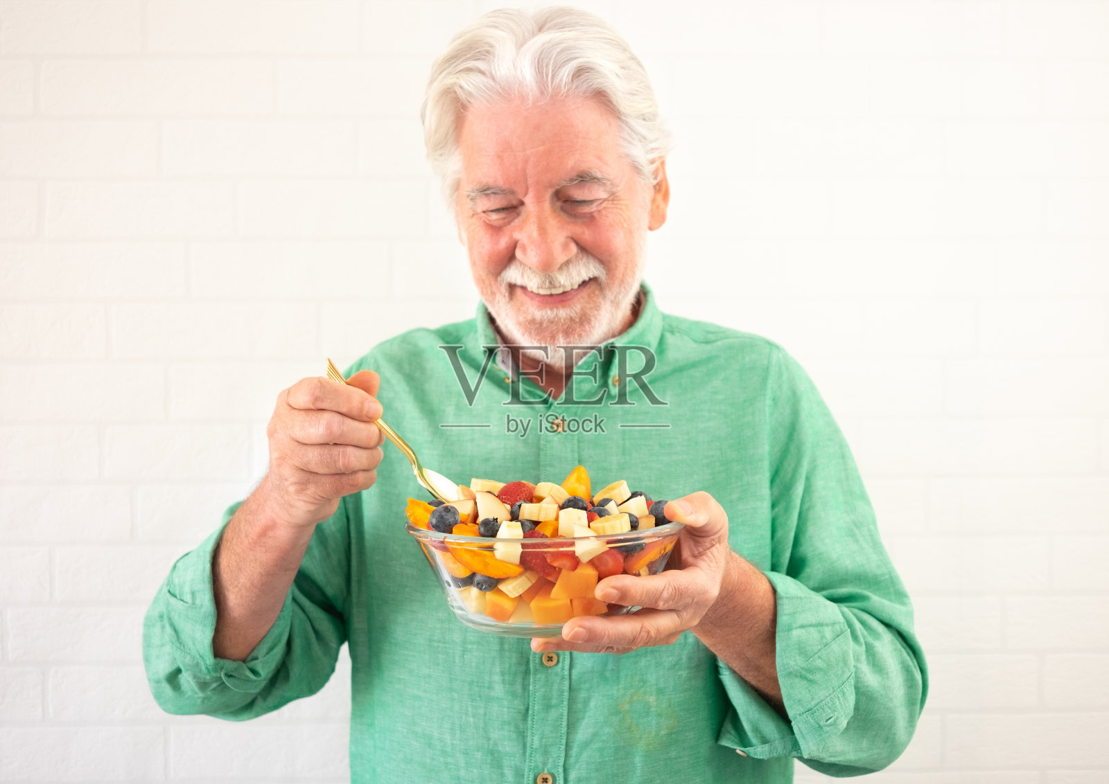 满脸笑容的大胡子老人捧着一碗新鲜时令水果准备吃。早餐或午餐，吃得健康而有节制照片摄影图片
