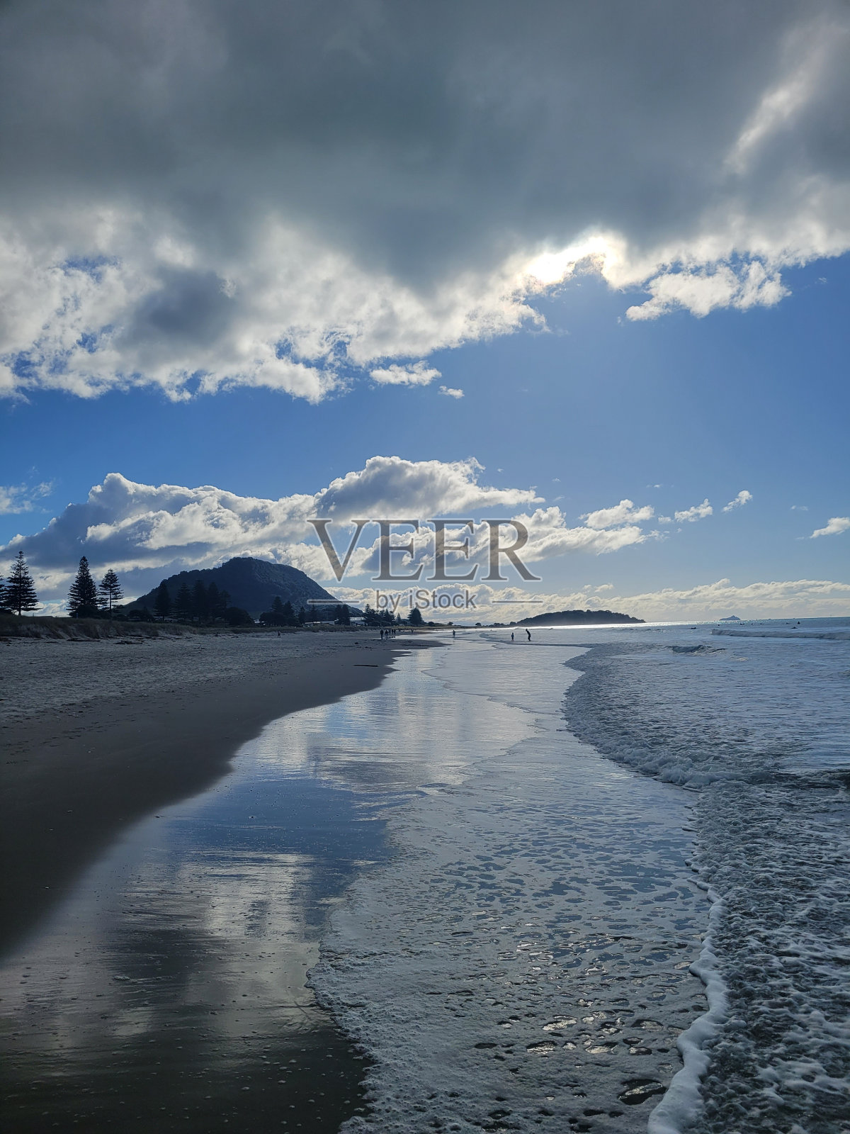 海滩上退去的海浪，阳光透过云层和山脉在背景中照射进来照片摄影图片