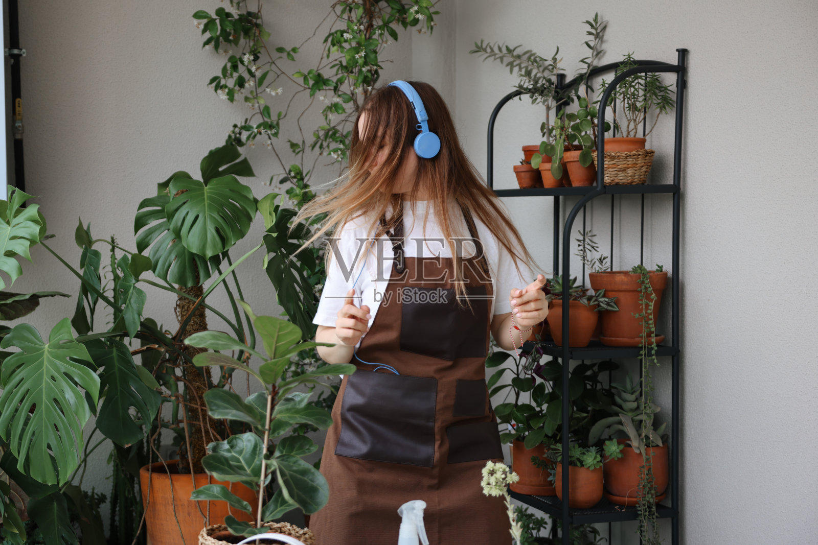 快乐的女人戴着无线耳机听着音乐，在家里的花园里跳着热带植物的舞照片摄影图片