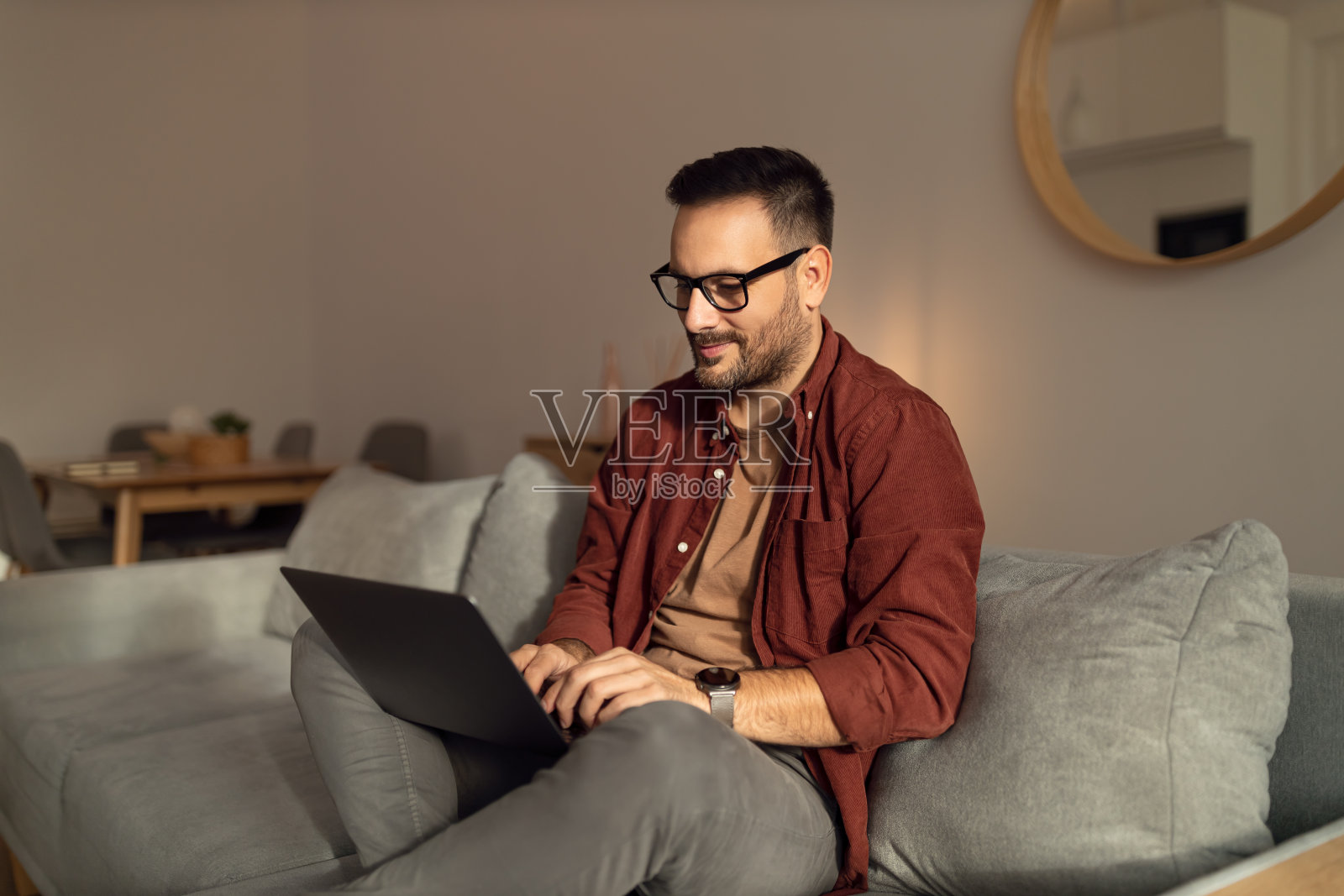 一个放松的人，坐在家里的沙发上，用着笔记本电脑，打着字。照片摄影图片