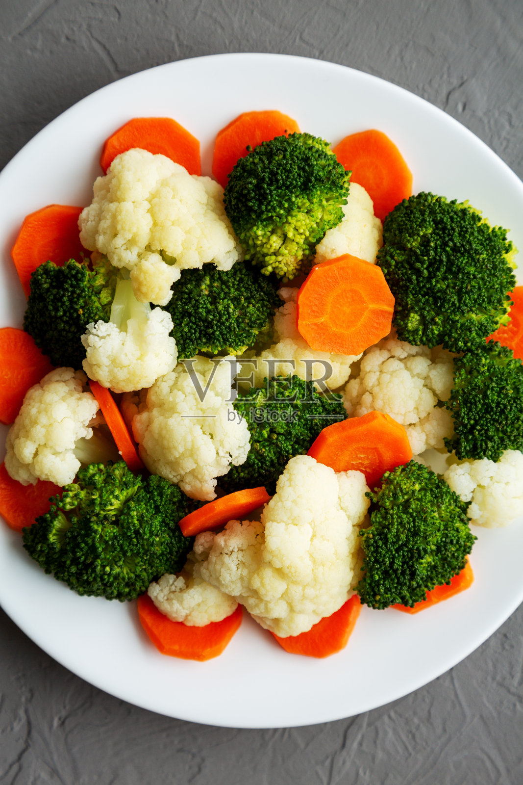 混合有机蒸蔬菜(胡萝卜，西兰花和花椰菜)在灰色背景上的一个盘子上，俯视图。平躺，头顶，从上面看。照片摄影图片