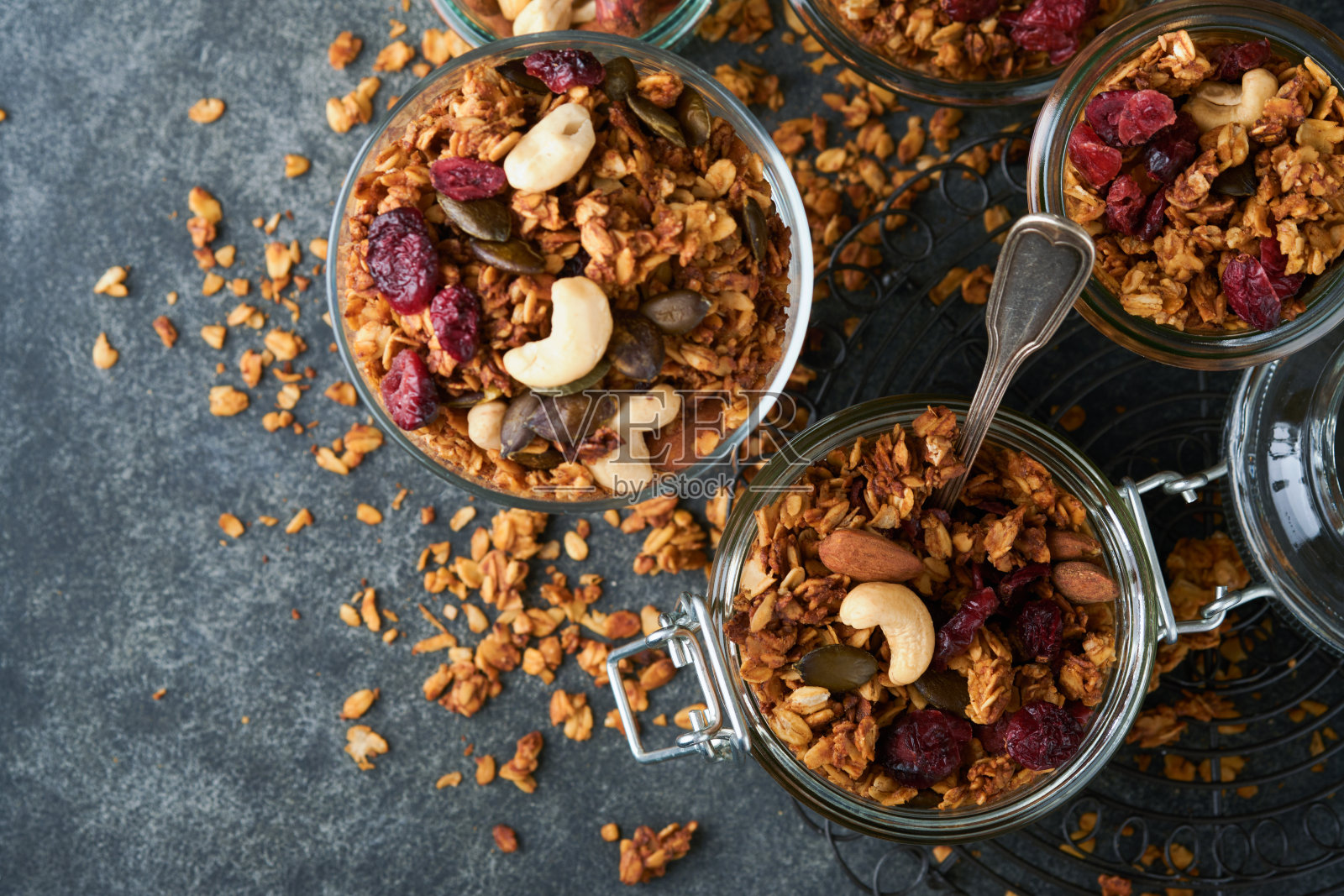 自制格兰诺拉麦片装在玻璃罐里，搭配希腊酸奶或牛奶、腰果、杏仁、南瓜和干蔓越莓籽，深灰色的餐桌背景。健康的能量早餐或零食。俯视图照片摄影图片
