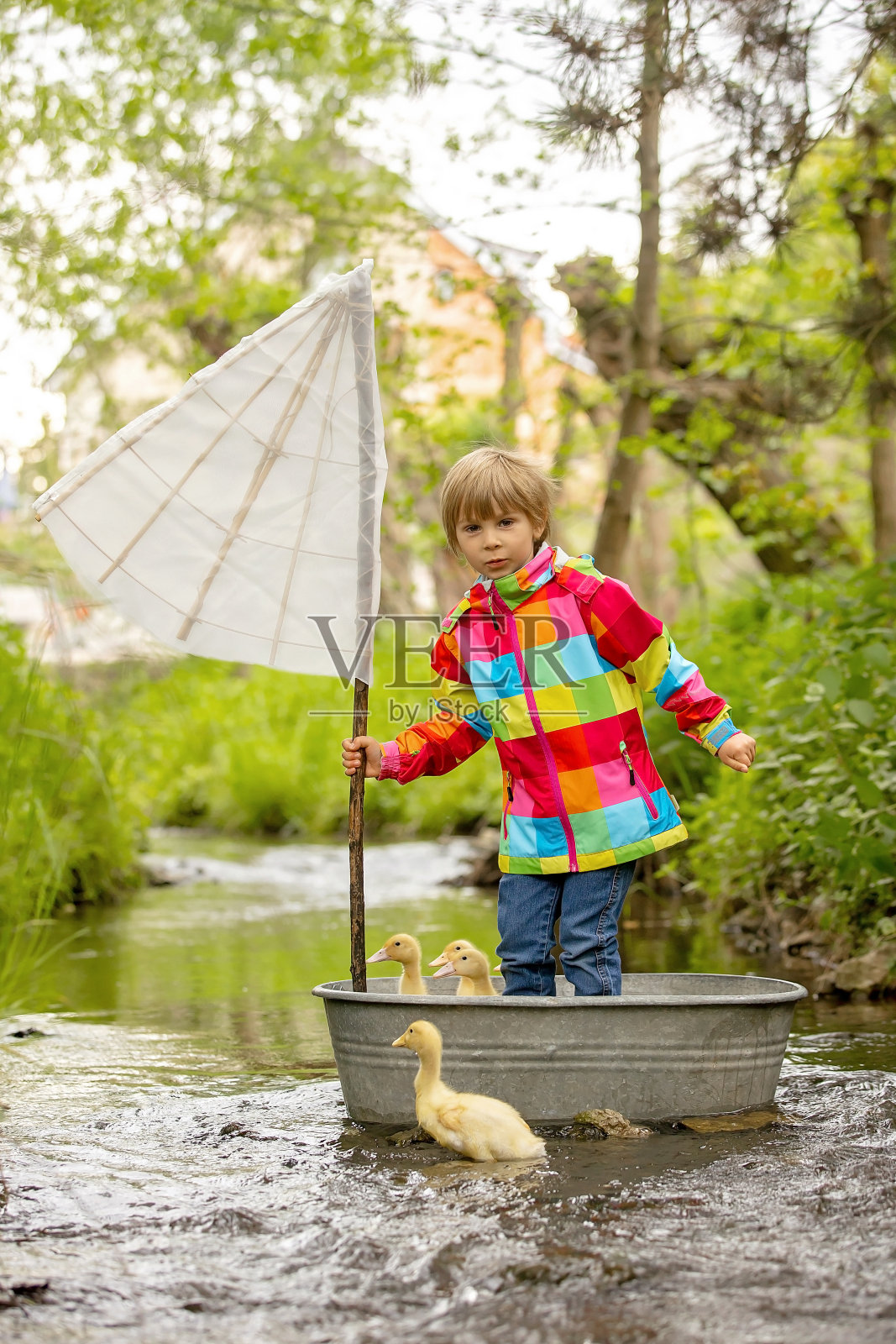 可爱的孩子，穿着彩色夹克的男孩，在一条小河上玩船和鸭子，帆船和划船。孩子玩得开心，童年的概念照片摄影图片