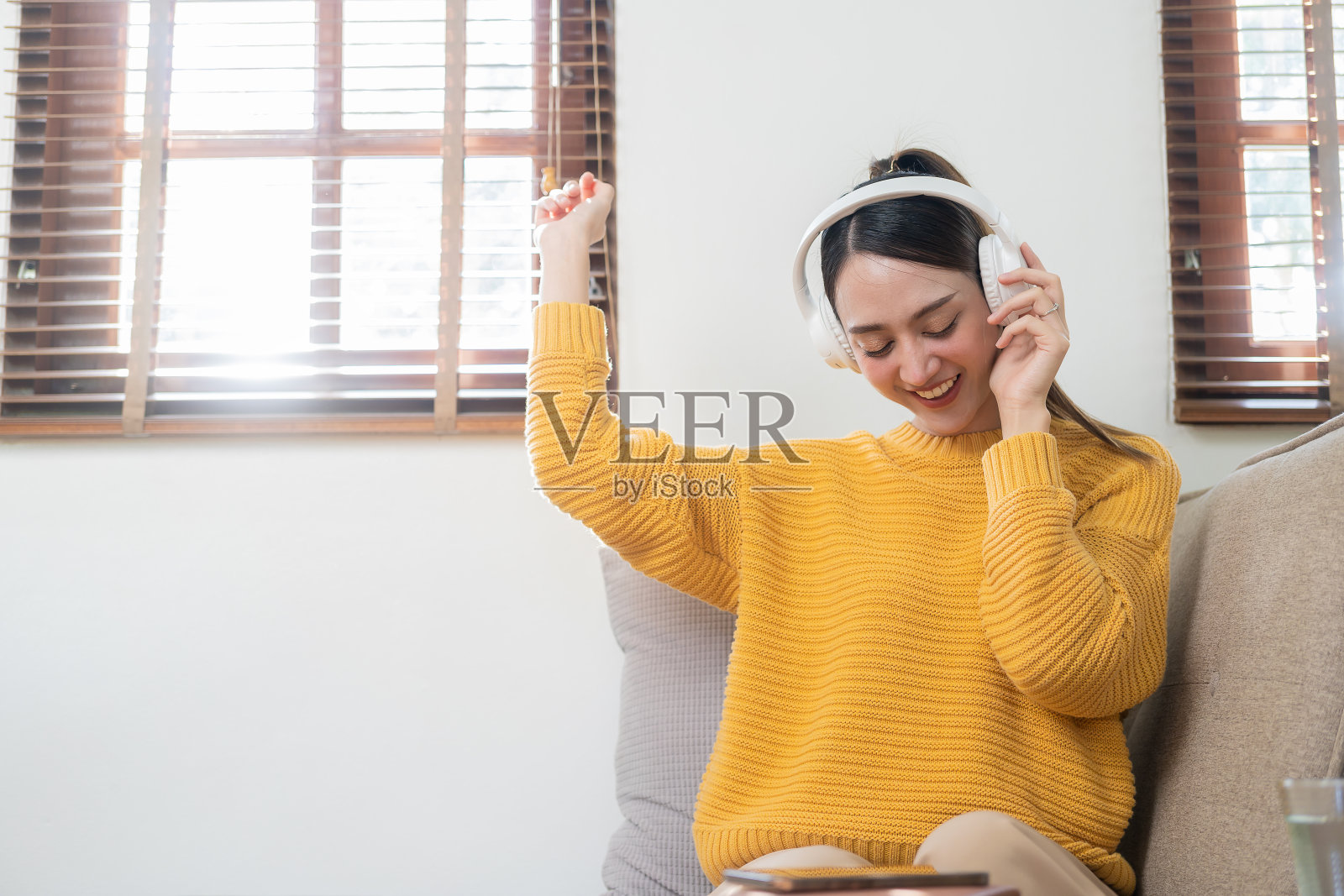 年轻漂亮的亚洲女孩，穿着黄色衬衫，快乐无忧无虑，戴着耳机，在客厅享受轻松的音乐，周末在家。照片摄影图片