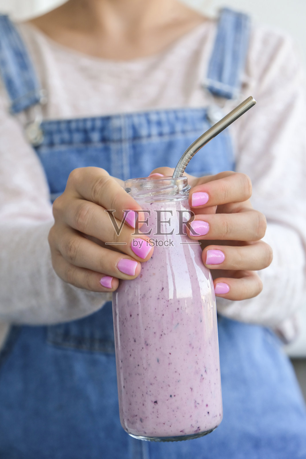 女性手里拿着蓝莓奶昔，上面放着蓝莓。女人吃一杯蛋白质奶昔早餐饮料由生蓝莓泥，香蕉，牛奶，酸奶和白软干酪制成照片摄影图片