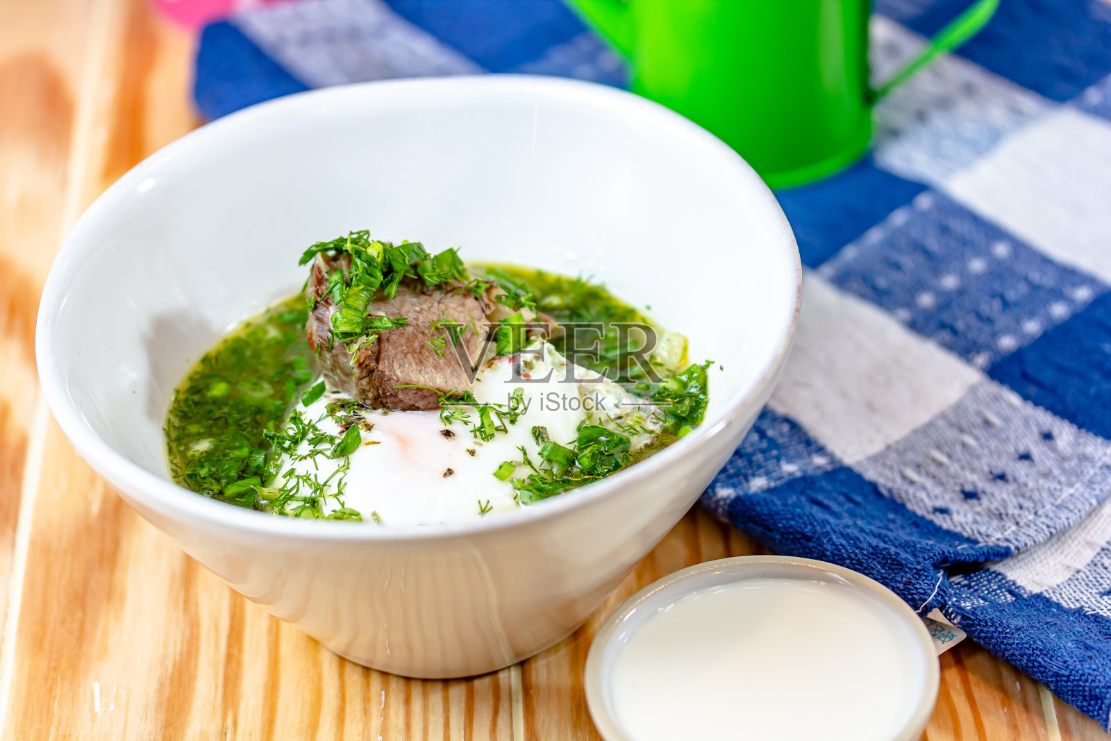 在木板上的白碗里盛有鸡肉、菠菜和鸡蛋的汤照片摄影图片