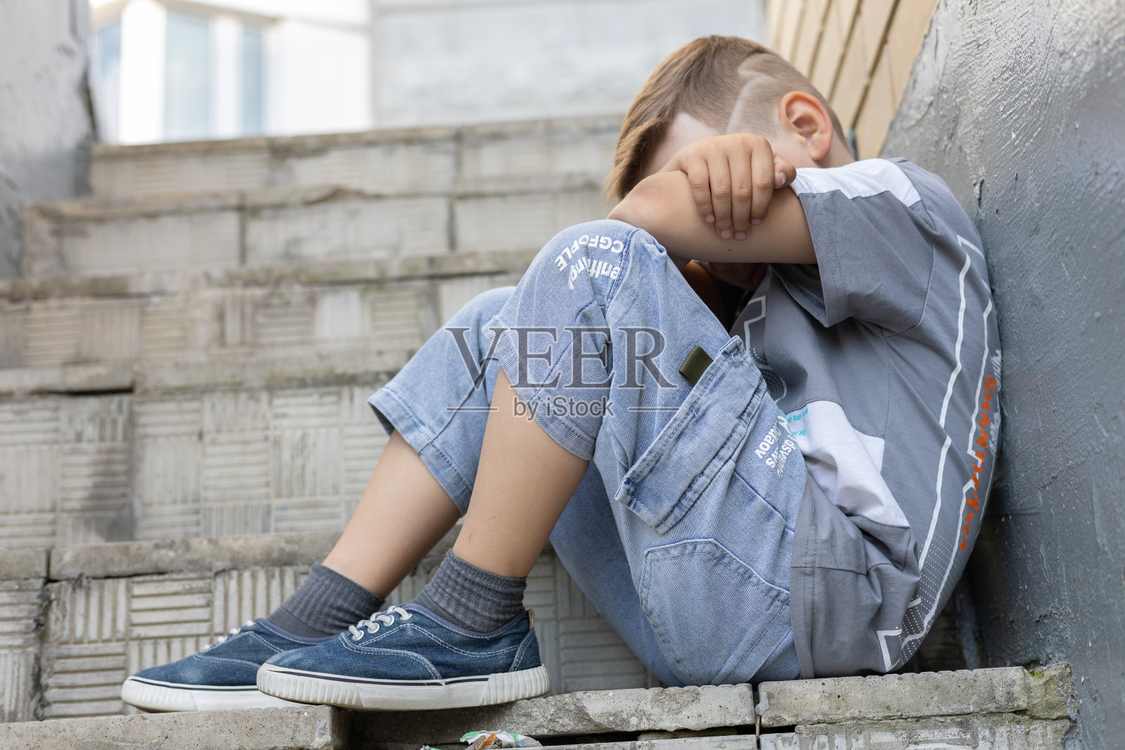 悲伤的男孩坐在街上的梯子上，双手抱膝的底部景观照片摄影图片