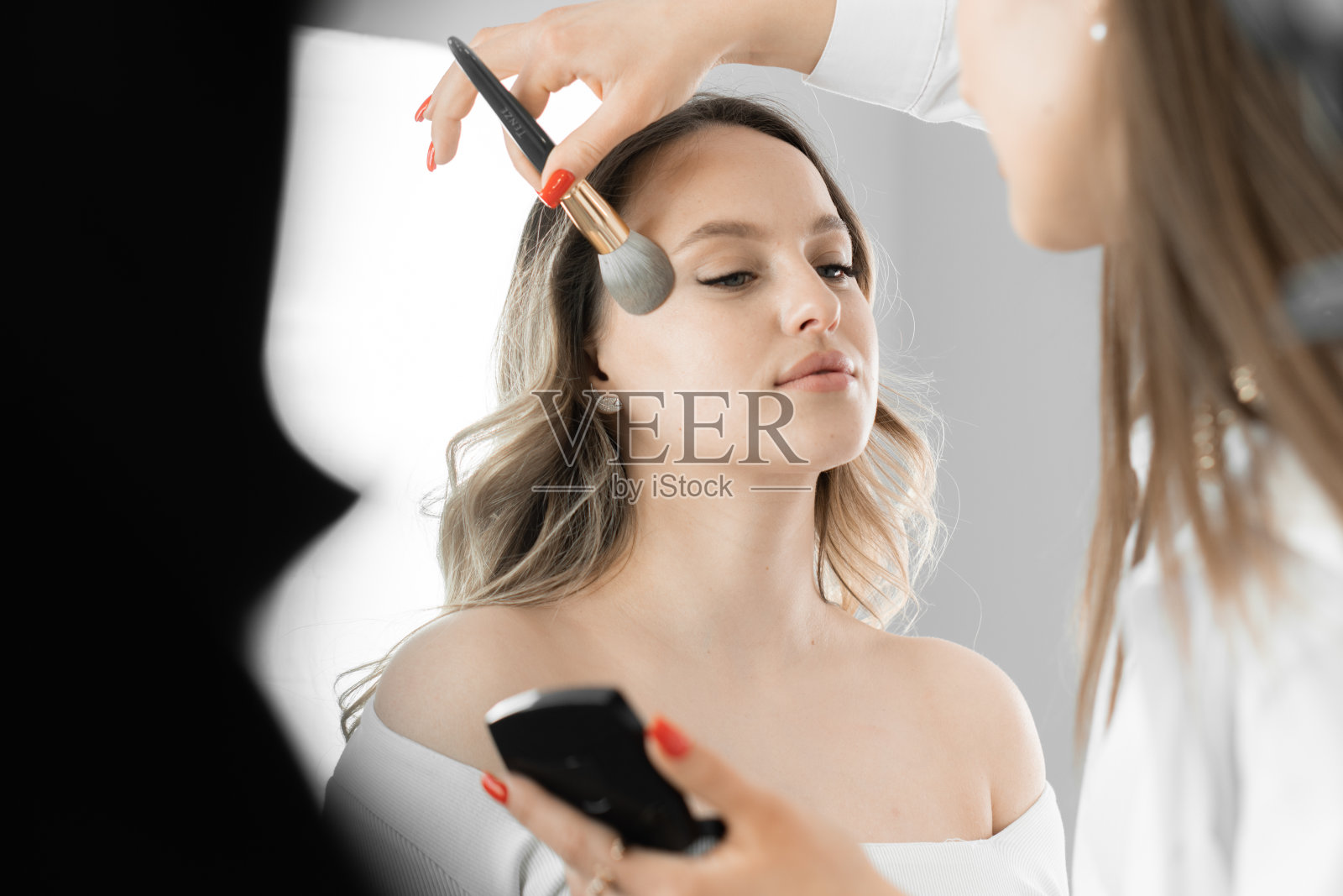 在高品质化妆品的帮助下，化妆师仔细关注自然美丽的年轻女性，帮助她闪耀着健康和清新。一位化妆师在他的脸上刷着刷子。照片摄影图片