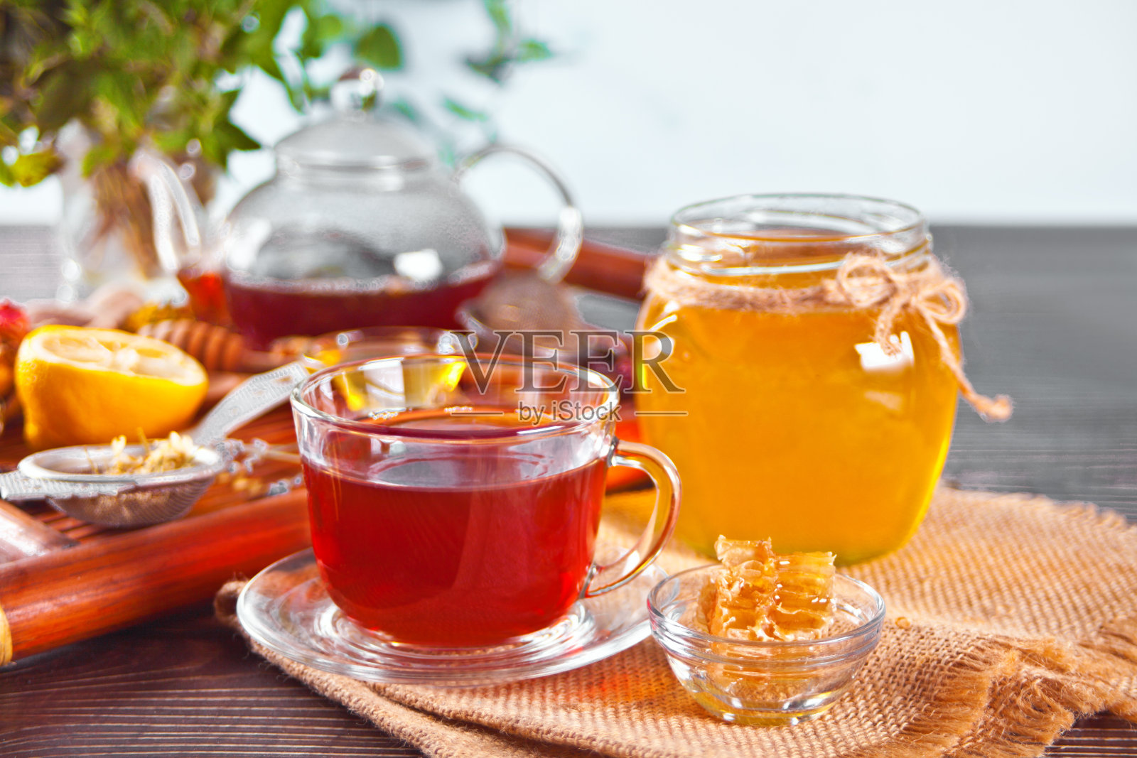 一杯花草茶，鲜花，蜂蜜在罐子里，茶壶和各种干燥的草药在托盘上。照片摄影图片