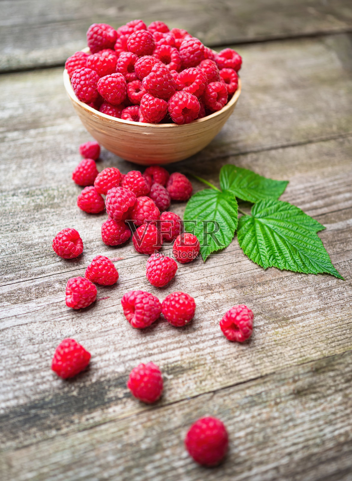 新鲜成熟的红覆盆子，叶子放在旧木桌上的碗里。照片摄影图片