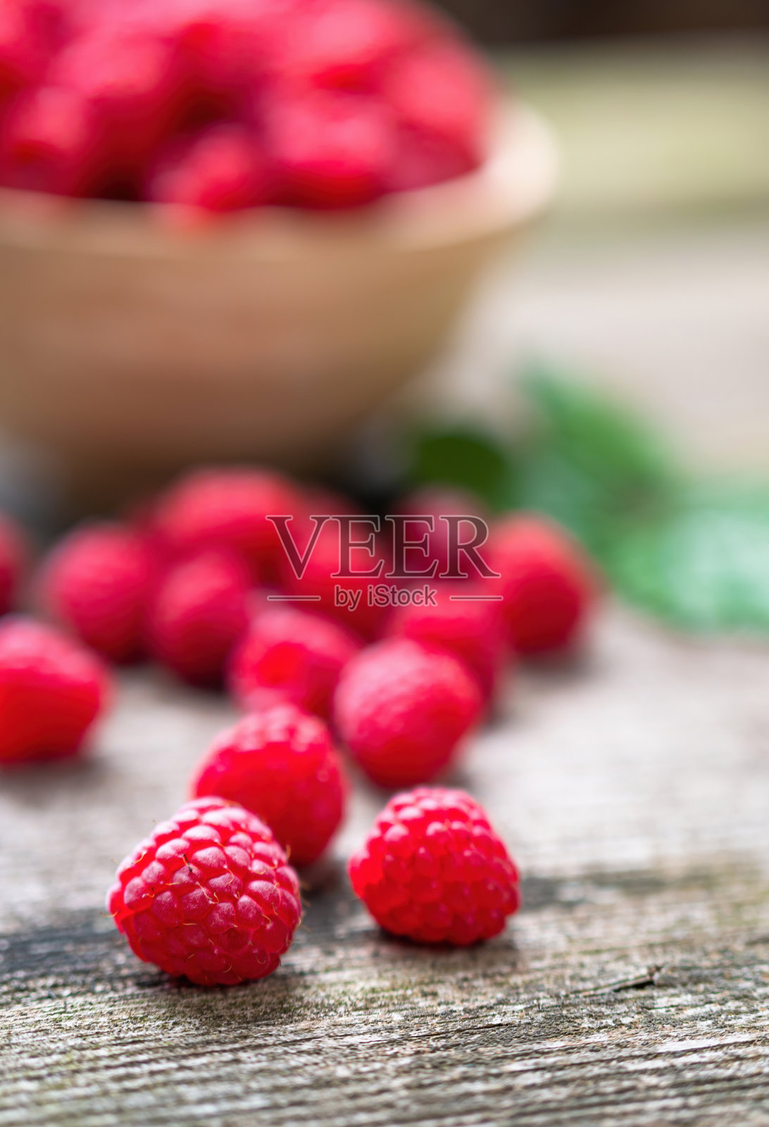 新鲜成熟的红覆盆子，叶子放在旧木桌上的碗里。照片摄影图片