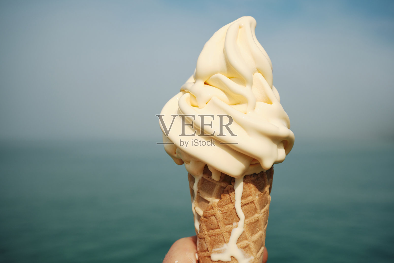 六月晴朗的一天，康沃尔郡纽基，美味的融化香草甜筒俯瞰着散焦的大海。照片摄影图片