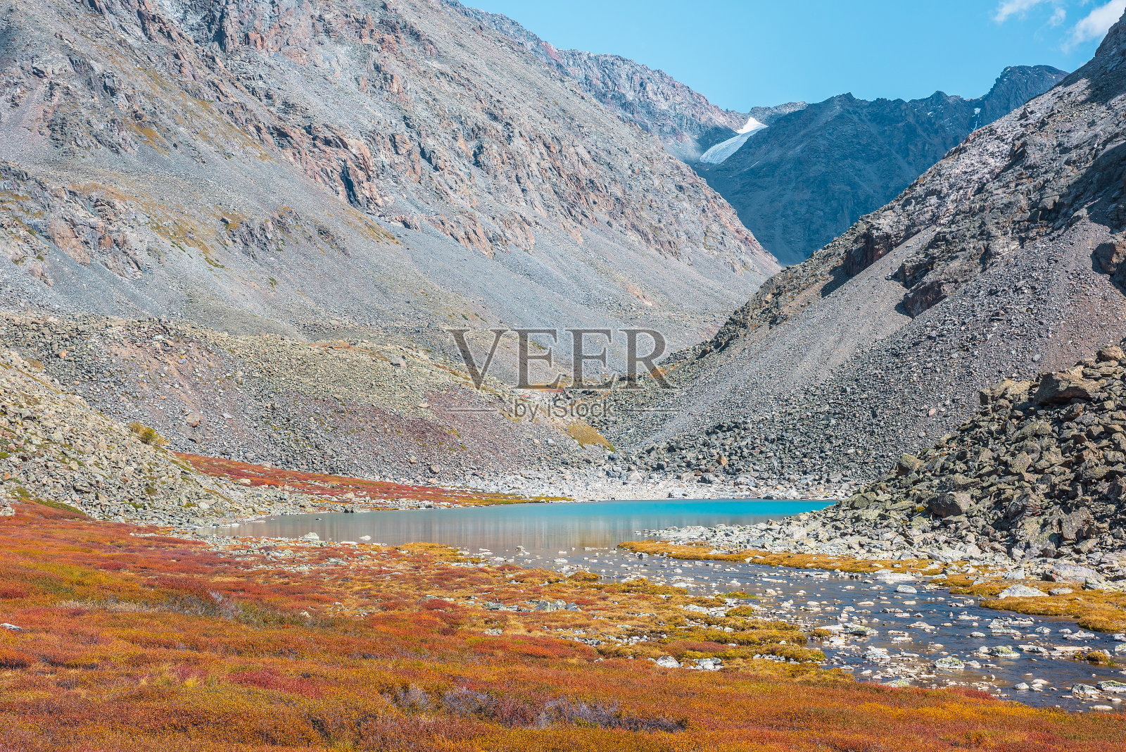 蔚蓝的小湖在多色的高山山谷中，在阳光明媚的日子里，岩石之间的秋天色彩鲜艳。浅石质的河流从山湖中间的斑驳矮桦树灌木在明亮的阳光在秋天照片摄影图片