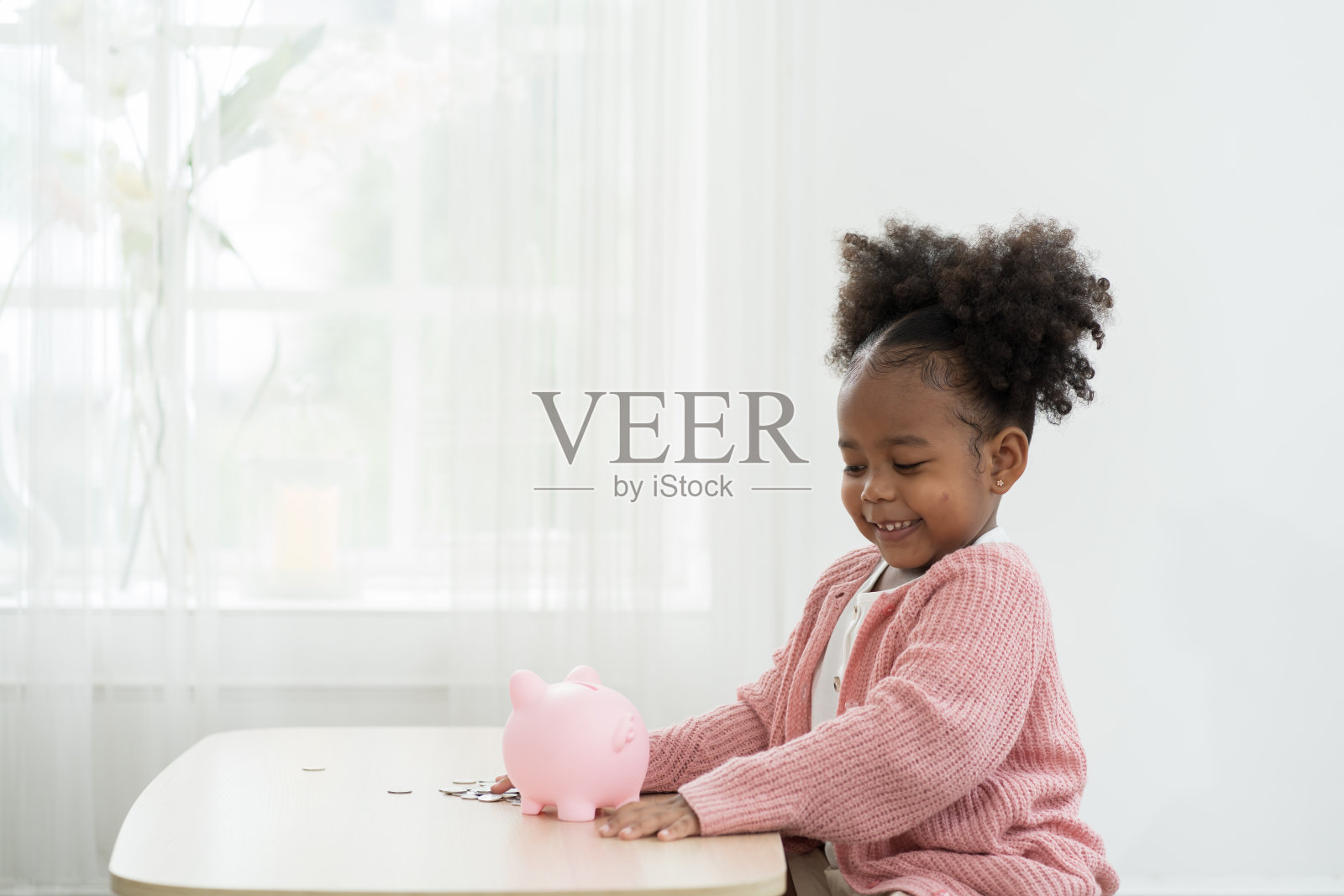 储蓄和银行理财的概念。小女孩往储蓄罐里存钱。非洲裔美国小女孩把一枚硬币放进存钱罐里。儿童投资未来概念照片摄影图片