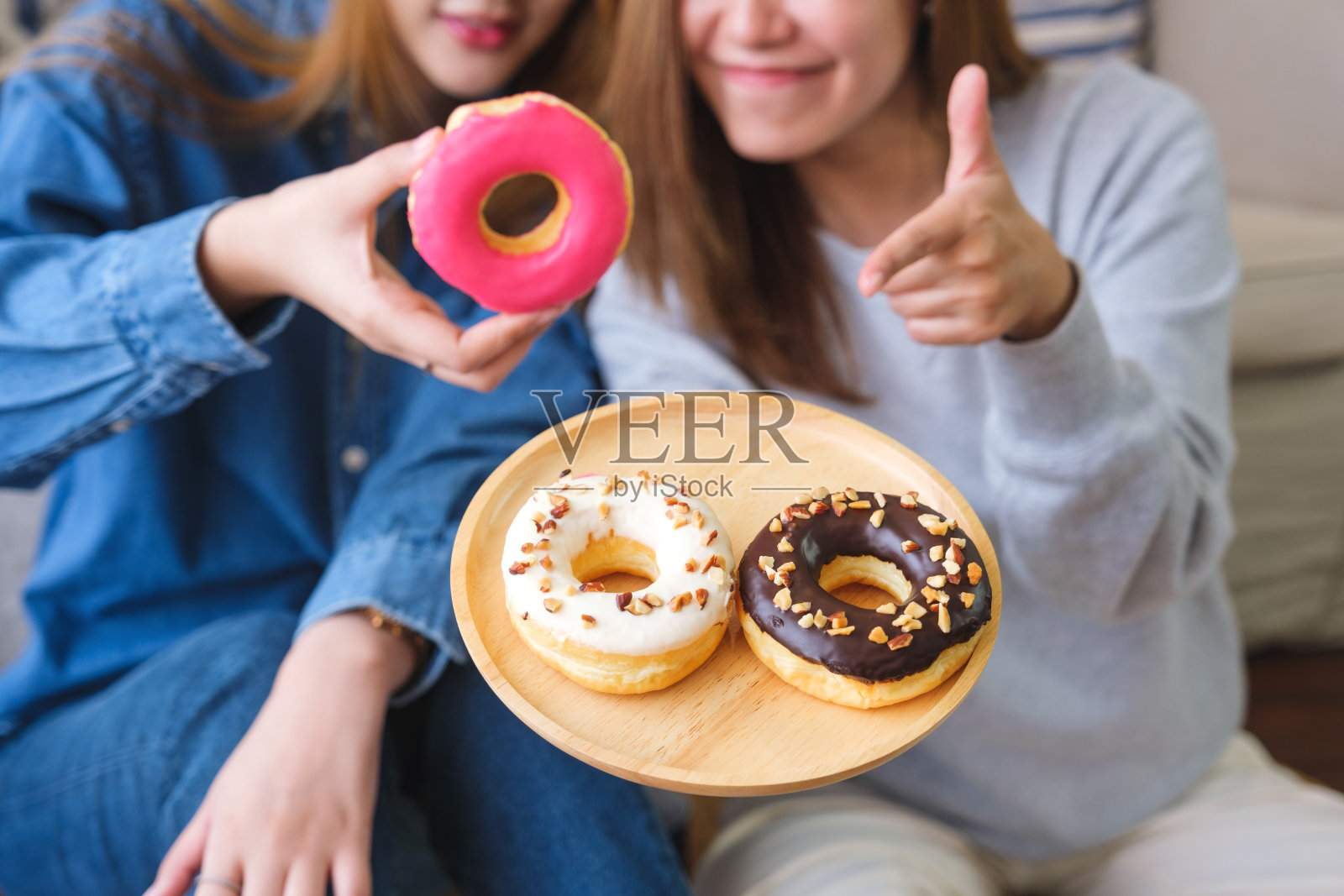 一对年轻夫妇的特写照片，她们拿着甜甜圈，用手指着甜甜圈照片摄影图片