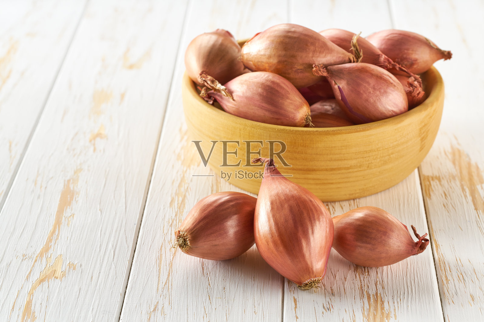 白色桌子上的木碗里放着葱头，为文字留出空间。照片摄影图片