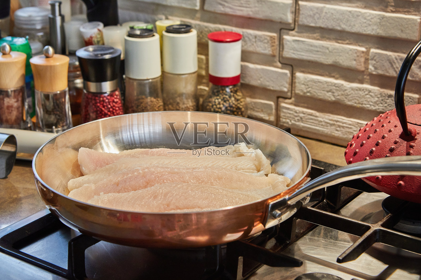 在燃气灶上的铜锅中煎炸鲈鱼照片摄影图片