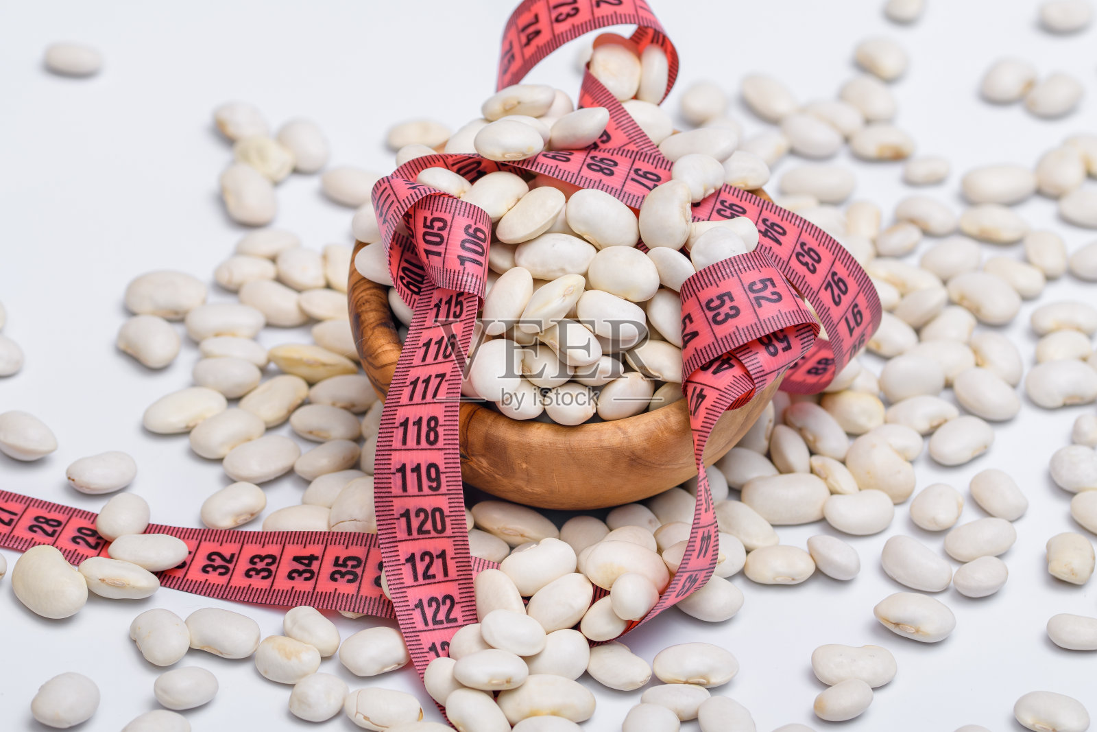 饮食白豆，散落在一个木碗周围，周围是卷尺，卷尺照片摄影图片