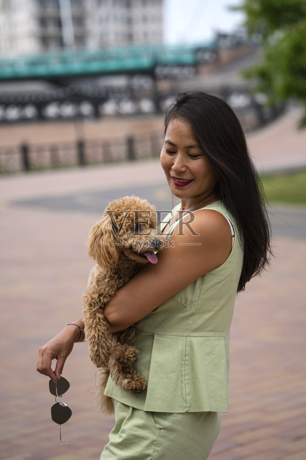 一个美丽的亚洲女孩(哈萨克)手里拿着一只狗(迷你贵宾犬)。这个女孩脸上流露出幸福和喜悦的表情。照片摄影图片