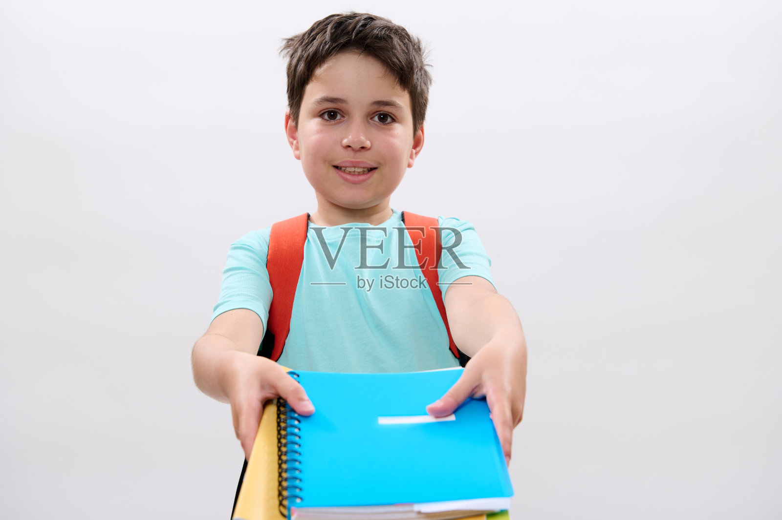 聪明的男生背着橙色的双肩包，在镜头前拿出课本和学习用品，孤立的白色背景照片摄影图片