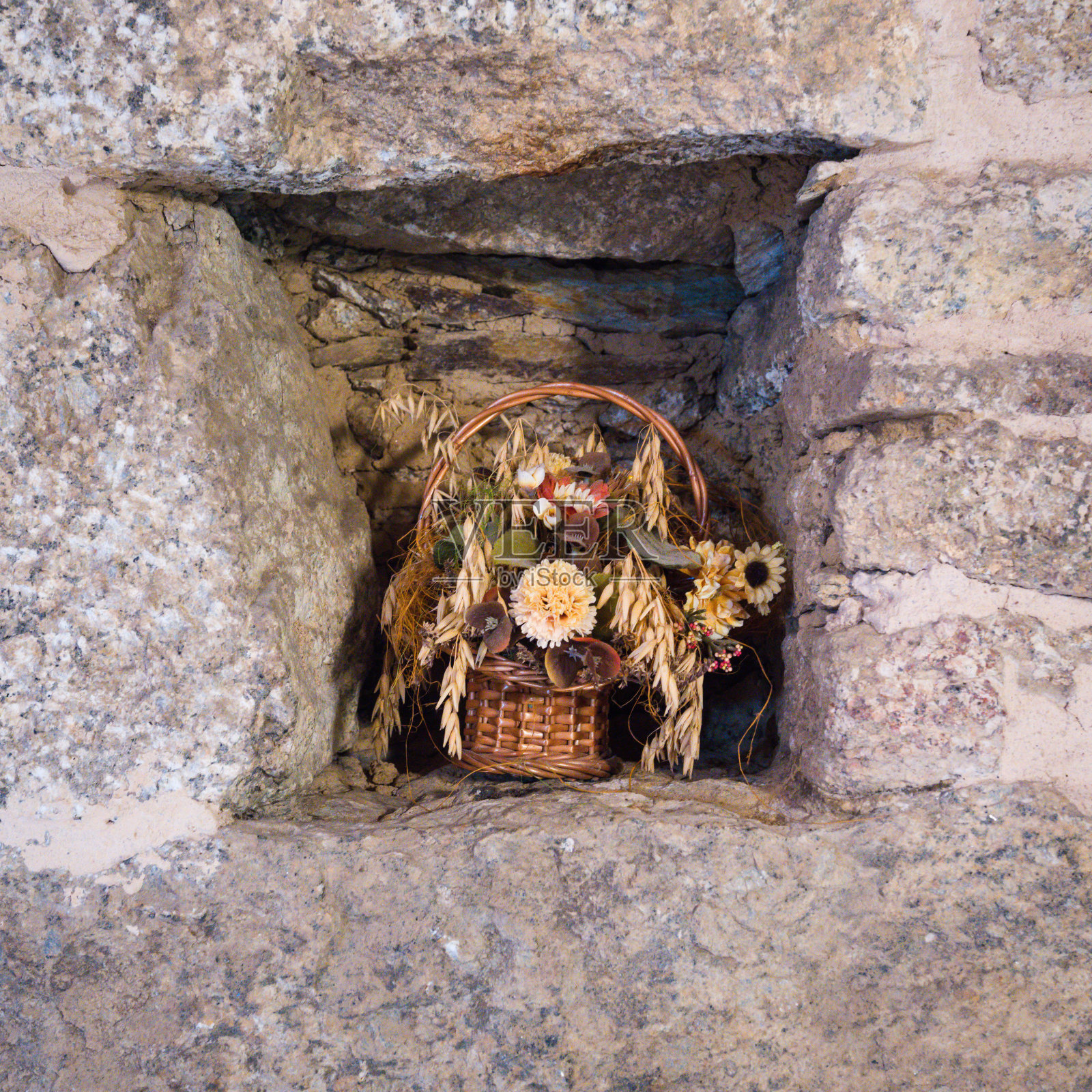 在一所乡村房屋的墙洞里摆放着干花的篮子照片摄影图片