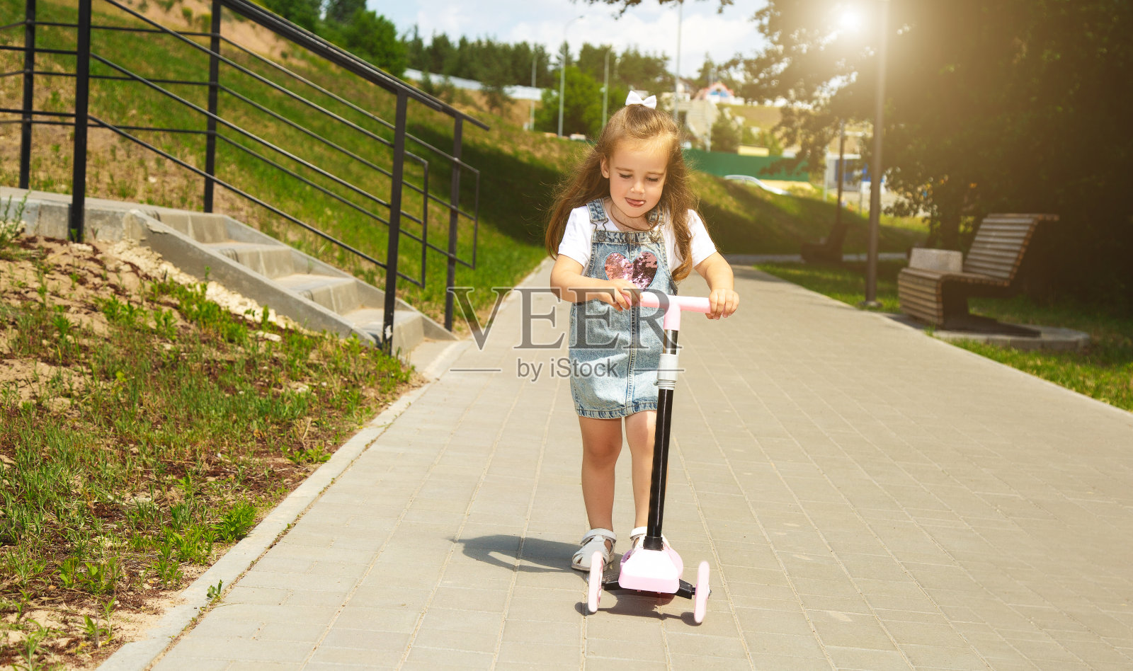 季节性儿童运动。健康的童年生活方式。暑假。小女孩，孩子骑着摩托车在公园外面的路上。照片摄影图片