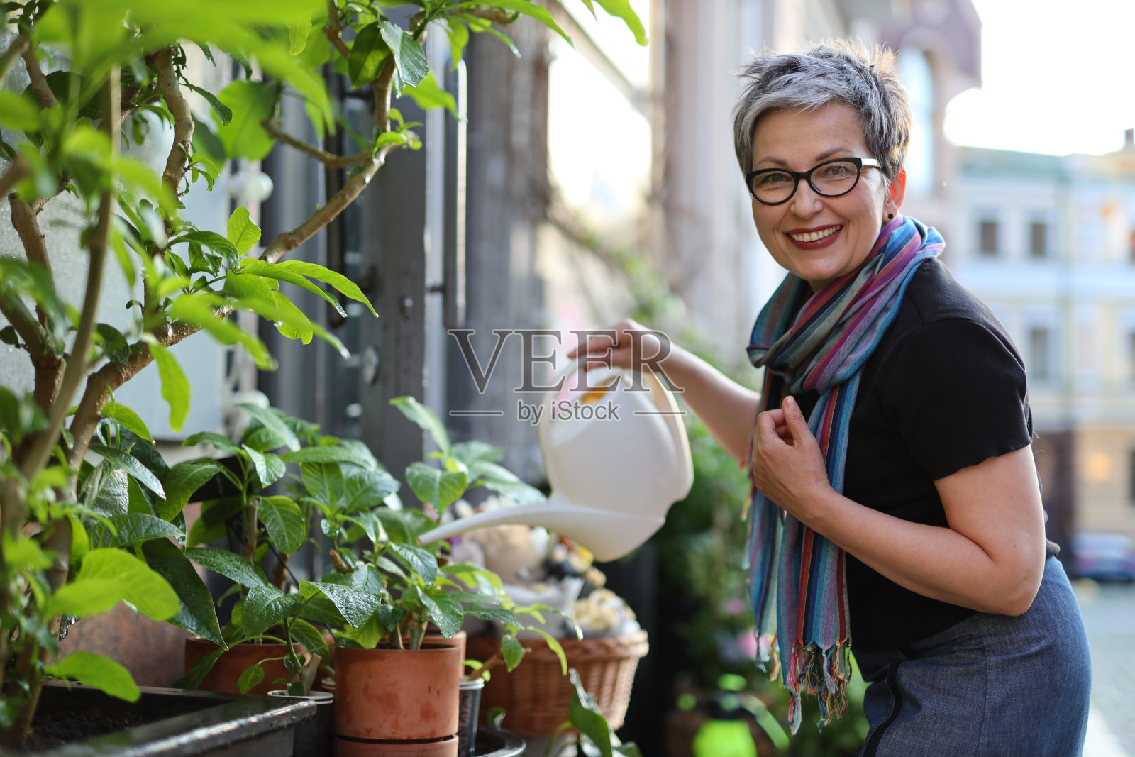 时尚的成年女子在花店附近的花坛里浇花。照片摄影图片