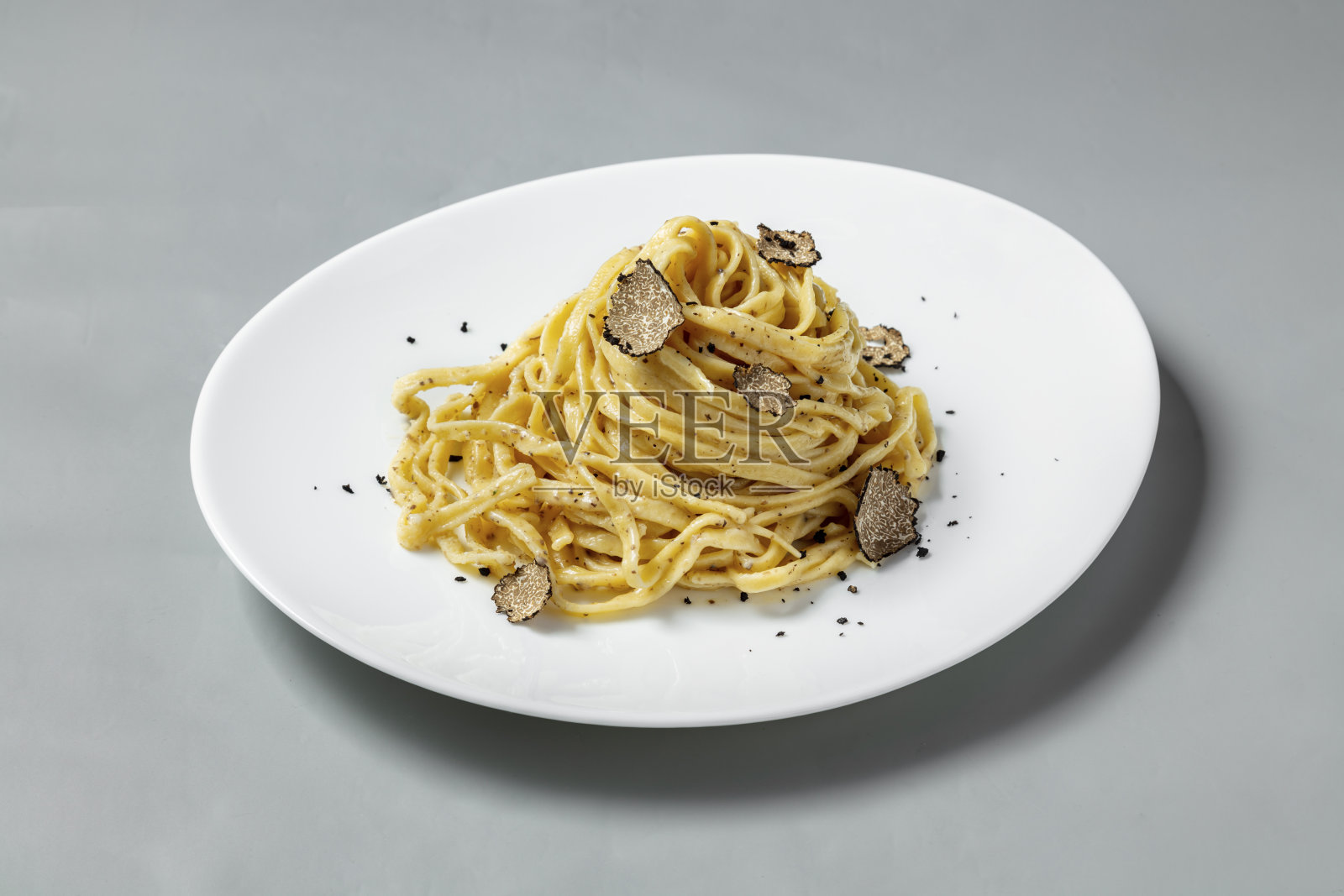 在灰色背景下，一个轻陶瓷盘子上放着松露蘑菇片的自制意大利面。照片摄影图片