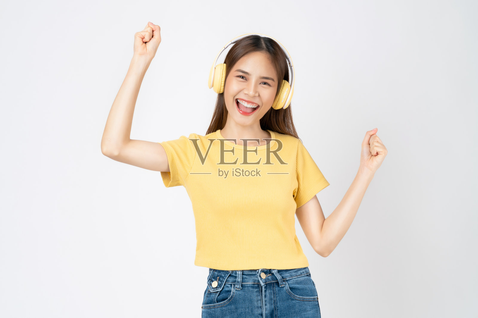 欢快的年轻亚洲妇女戴着耳机听音乐，享受最喜欢的播放列表应用程序，在粉红色的背景上跳舞。照片摄影图片