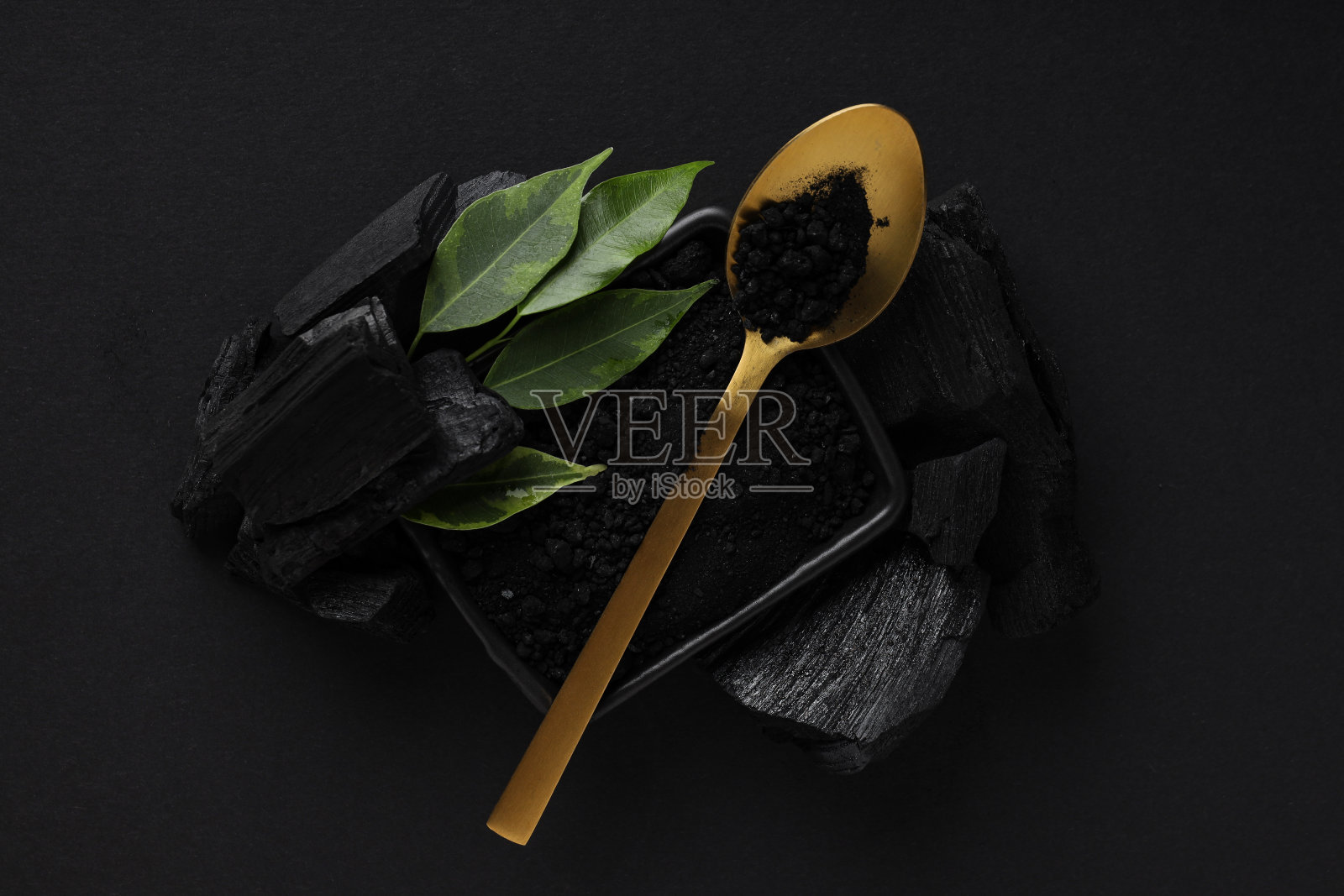 木炭，木炭粉，勺子和黑色背景的叶子照片摄影图片