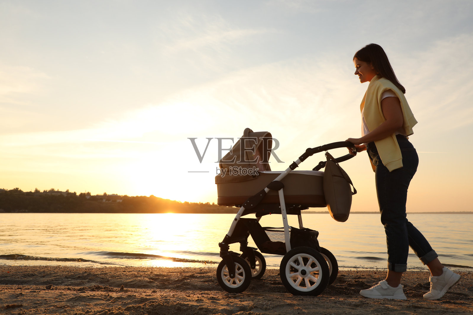 快乐的妈妈和宝宝在河边散步在日落照片摄影图片