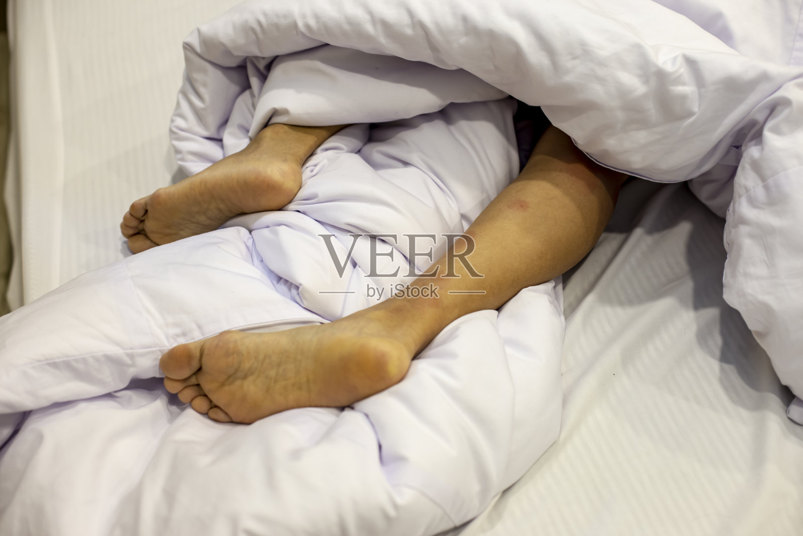 从白色毯子下伸出的双脚照片摄影图片