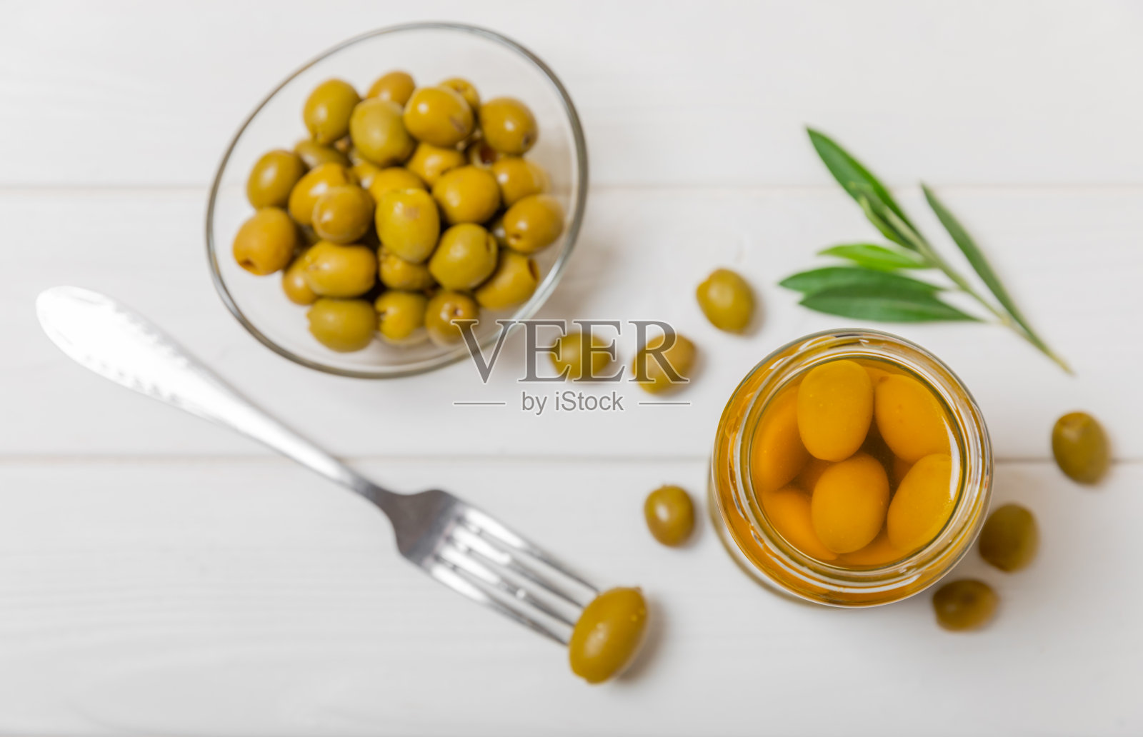 白色木制背景上的玻璃罐子里装着橄榄。罐子里去核的绿橄榄。玻璃罐里的腌橄榄。在木制背景上。腌橄榄。文本空间。拷贝空间。素食食物。照片摄影图片