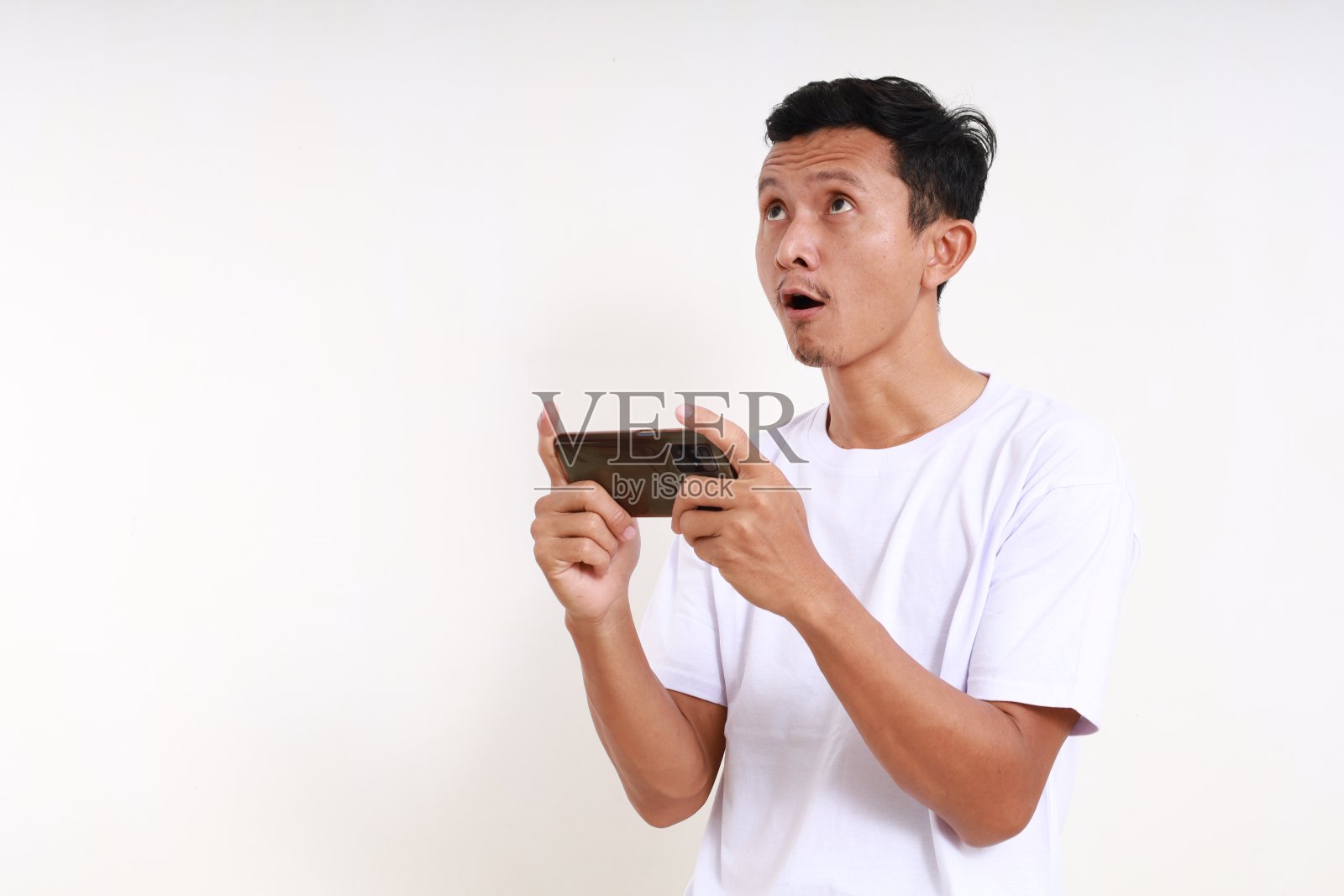 哇，亚洲滑稽男人一边玩智能手机一边看上面的表情。孤立的照片摄影图片