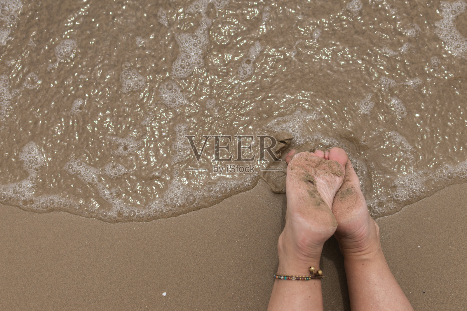 海滩岸边的沙滩上，一个女人的湿赤脚的脚。健康和幸福的概念，度假和旅游的海滨目的地。夏季海水照片摄影图片