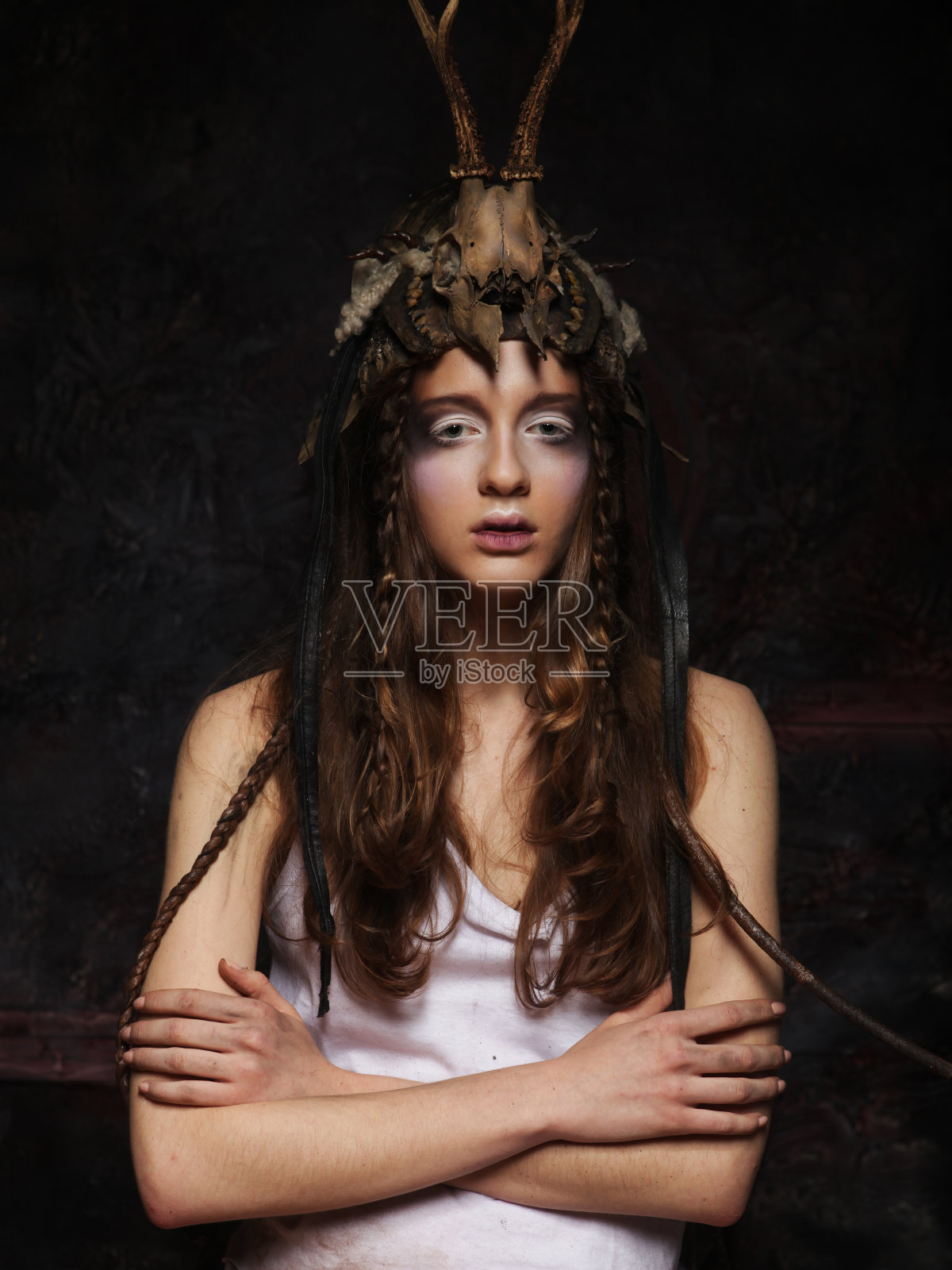 一名年轻女子画着鲜艳的妆容，梳着辫子，头戴骷髅头，双手交叉站着照片摄影图片