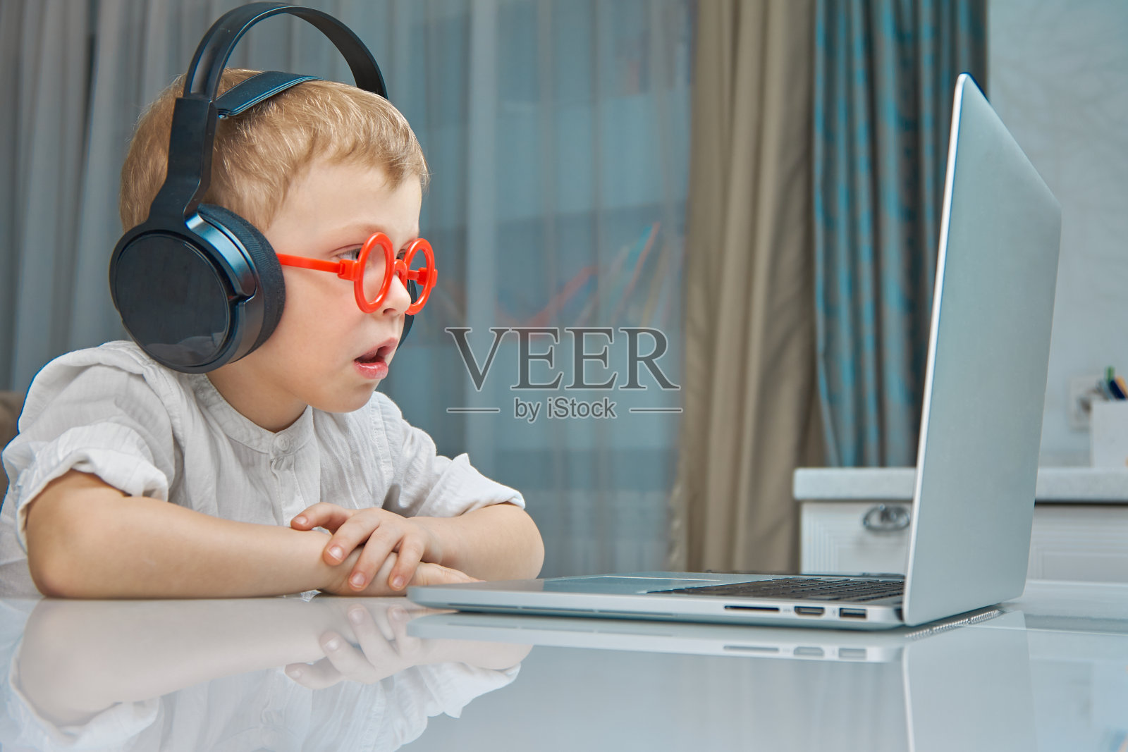 一个戴着红色眼镜和黑色耳机的男孩在研究这台笔记本电脑照片摄影图片