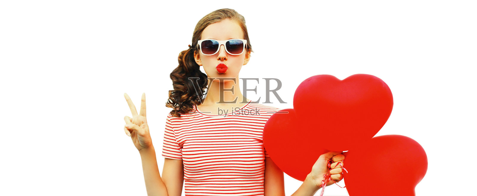 美丽的年轻女子的肖像与红色的心形状的气球吹她的嘴唇发送甜蜜的空气吻戴墨镜孤立在白色背景照片摄影图片