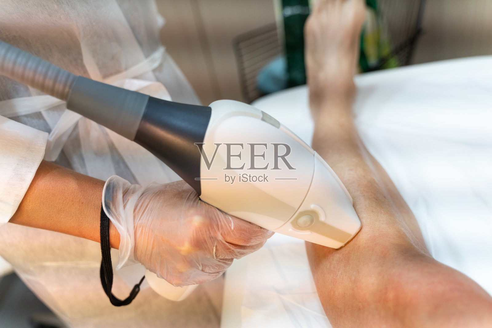 美容师的手应用激光脱毛枪的人的腿照片摄影图片