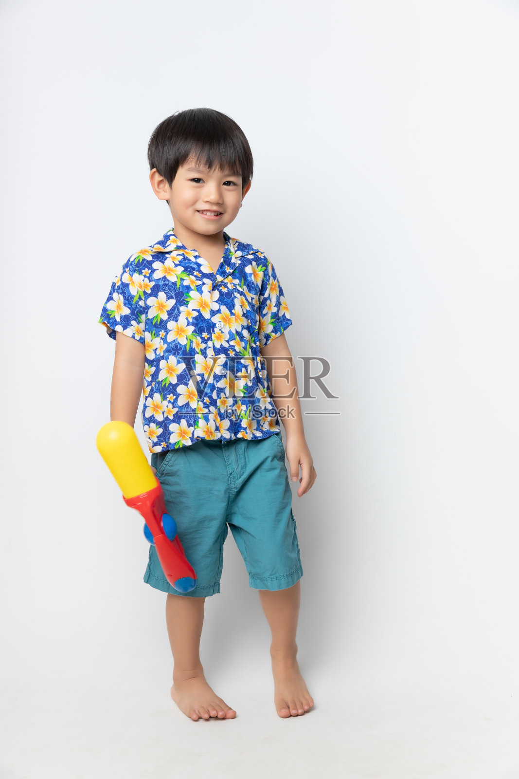 迎接泰国泼水节的亚洲男孩的肖像穿着花衬衫微笑着，白色背景上的水枪。照片摄影图片