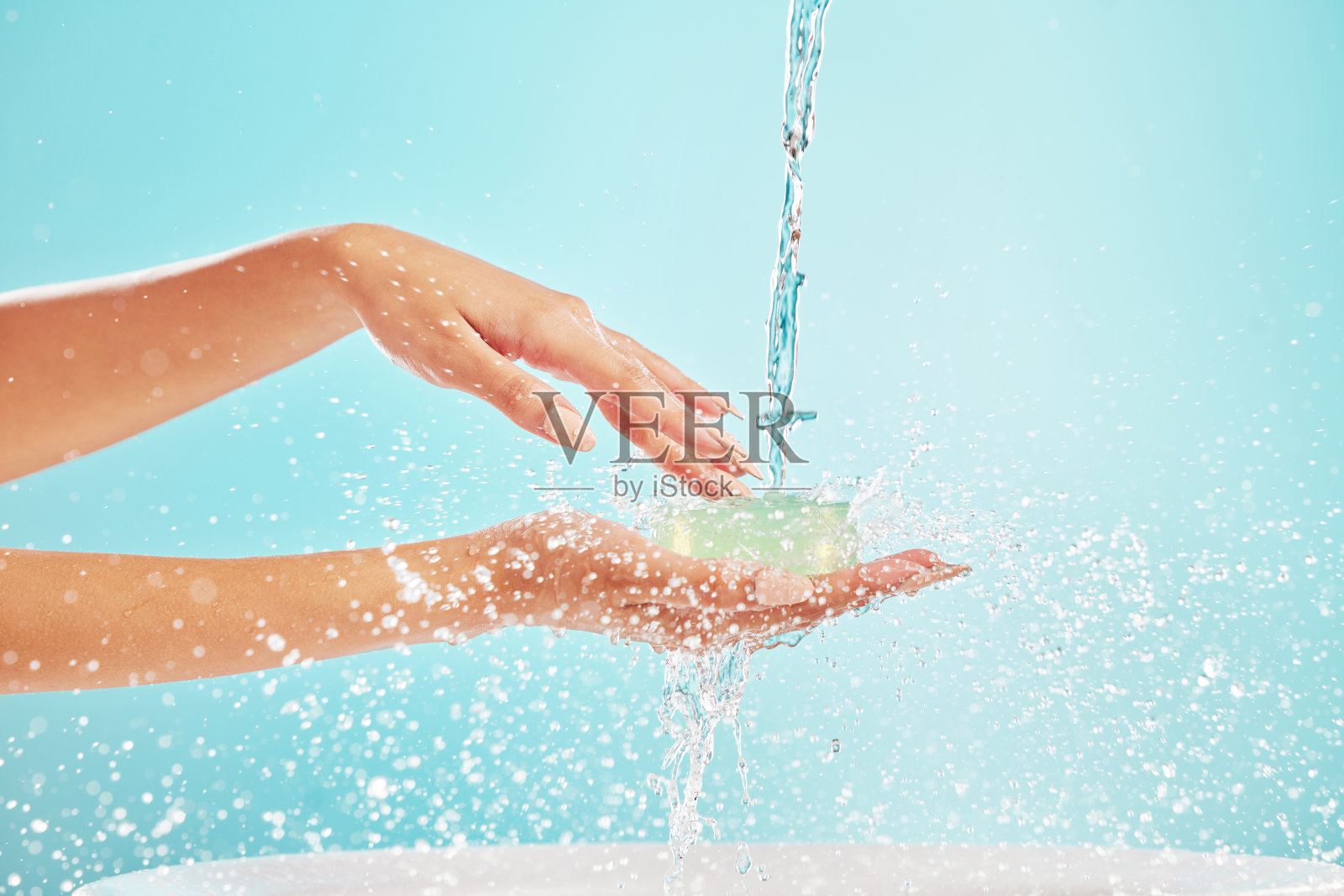 在摄影棚里，一个不知名的女人在蓝色背景下捧着她的手抓水照片摄影图片