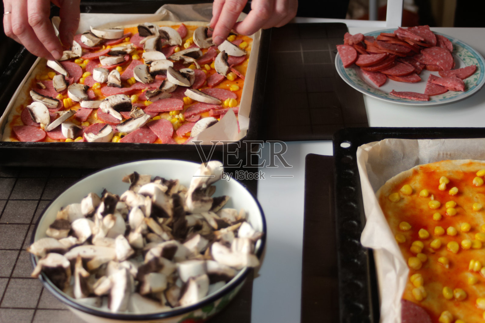 虚焦的披萨配料，女性手部正在烹饪，红色番茄酱、香肠、甜玉米、蘑菇，自制意大利披萨，玛格丽特披萨的基底，凌乱的桌子，家庭烹饪，焦外效果照片摄影图片