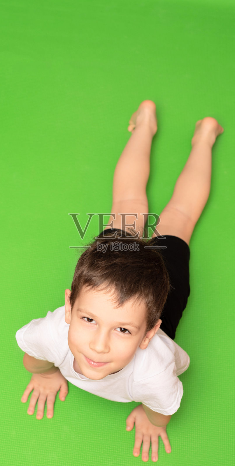 小男孩在绿色瑜伽垫上做体操。居家健身概念照片摄影图片