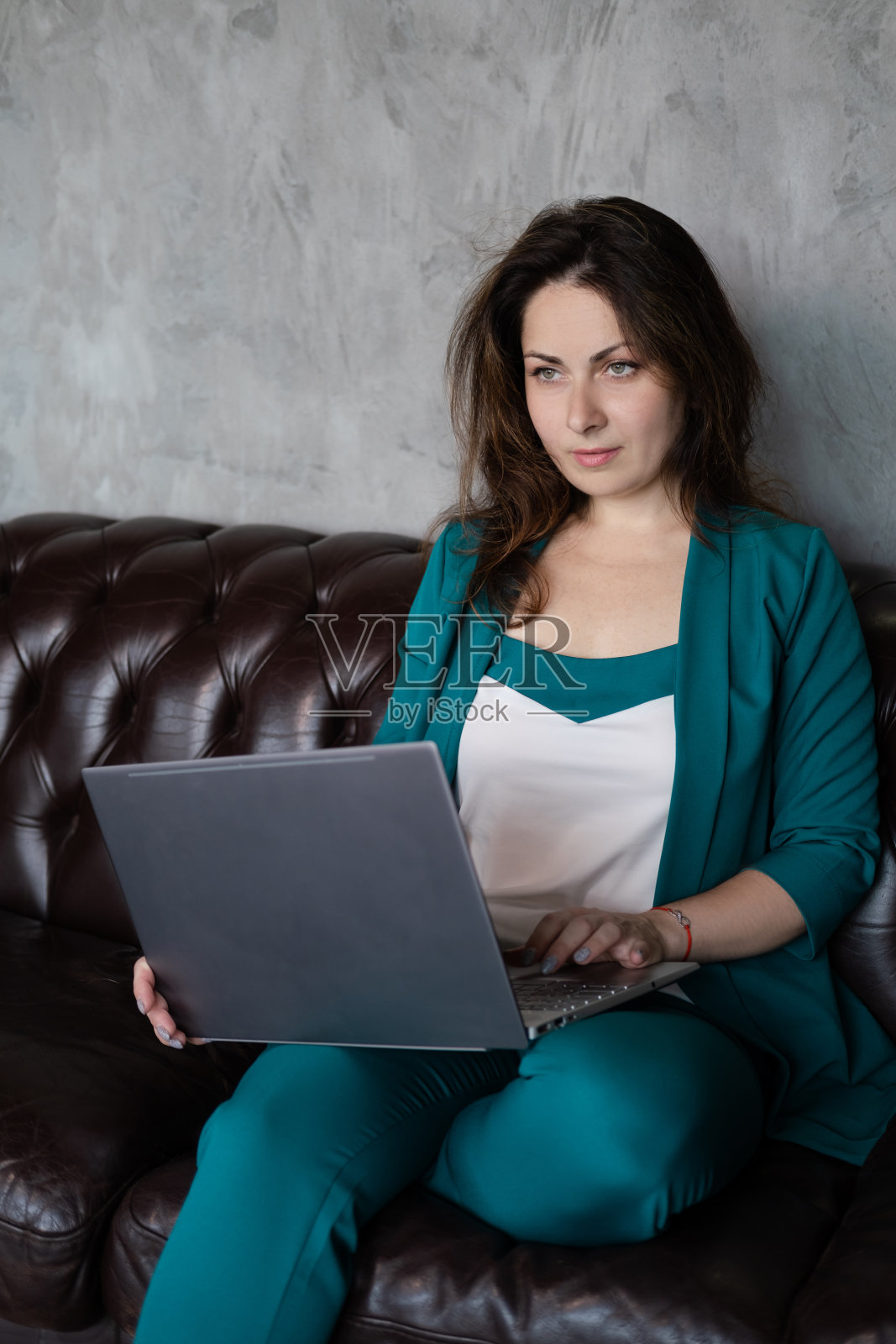 远程工作，远程教育。深褐色的女人在绿色皮革沙发上与笔记本电脑。家庭办公室。居家办公照片摄影图片