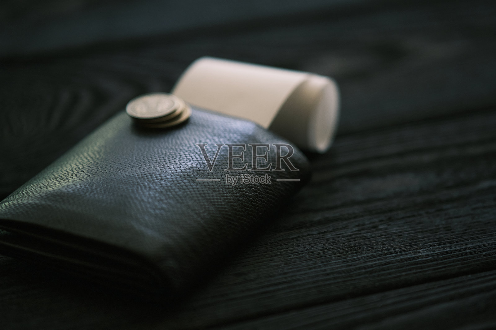 一个皮钱包和一小堆硬币放在黑色的木桌上照片摄影图片